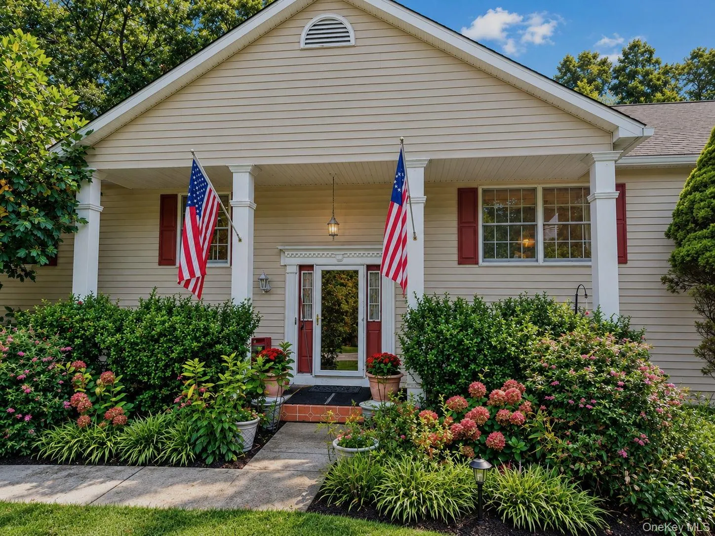 Cream-colored siding exterior with a covered porch, featuring decorative pillars and red window shutters Cream-colored siding exterior with a covered porch, featuring decorative pillars and red window shutters