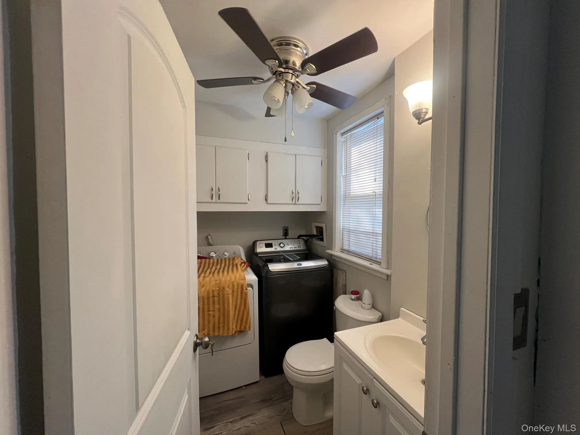 Integrated laundry area featuring upper cabinetry, a window with blinds, and wood-finish flooring half bathroom on first floor Integrated laundry area featuring upper cabinetry, a window with blinds, and wood-finish flooring half bathroom on first floor