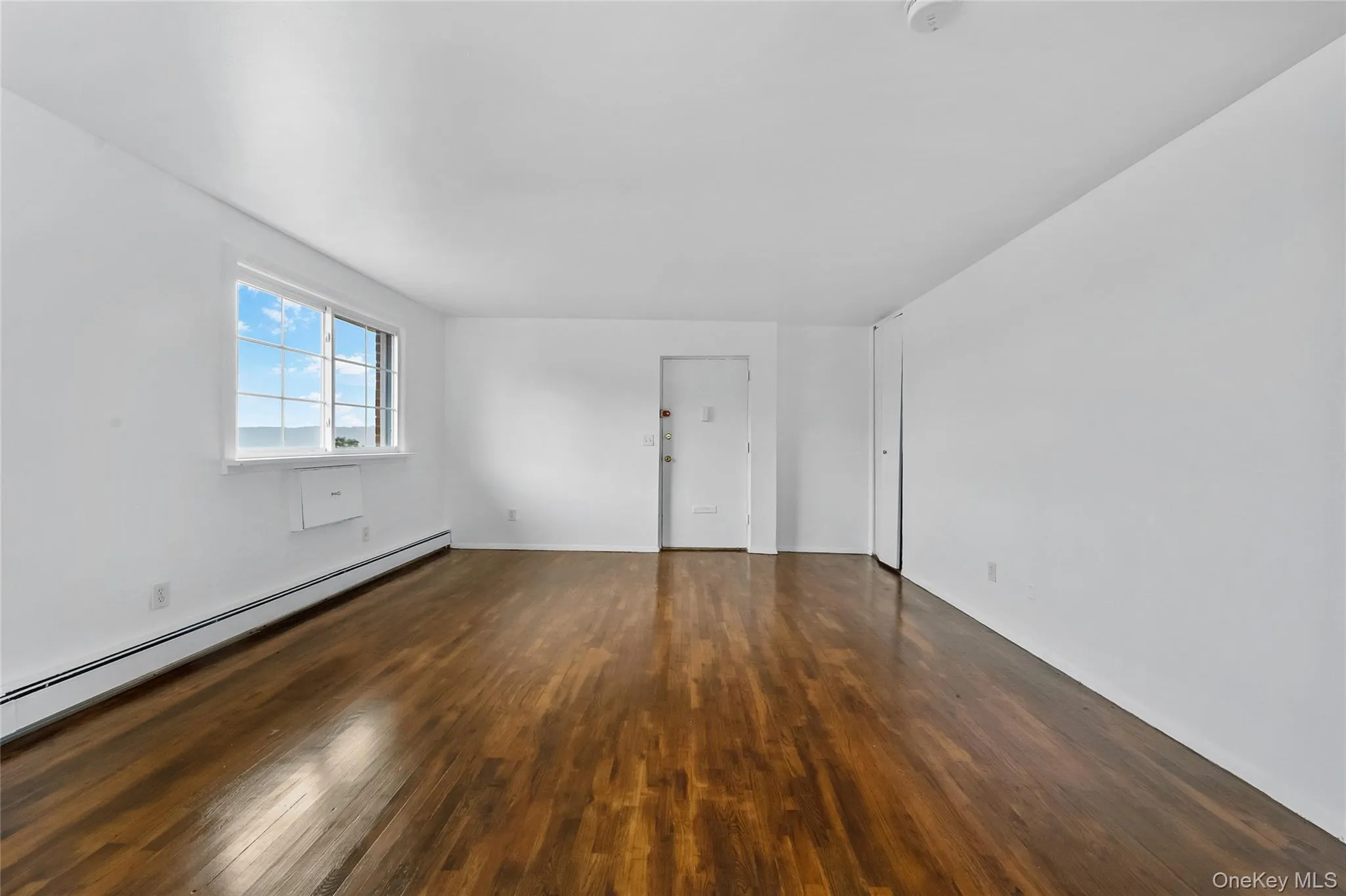 Unfurnished room featuring dark wood finished floors and baseboard heating Unfurnished room featuring dark wood finished floors and baseboard heating