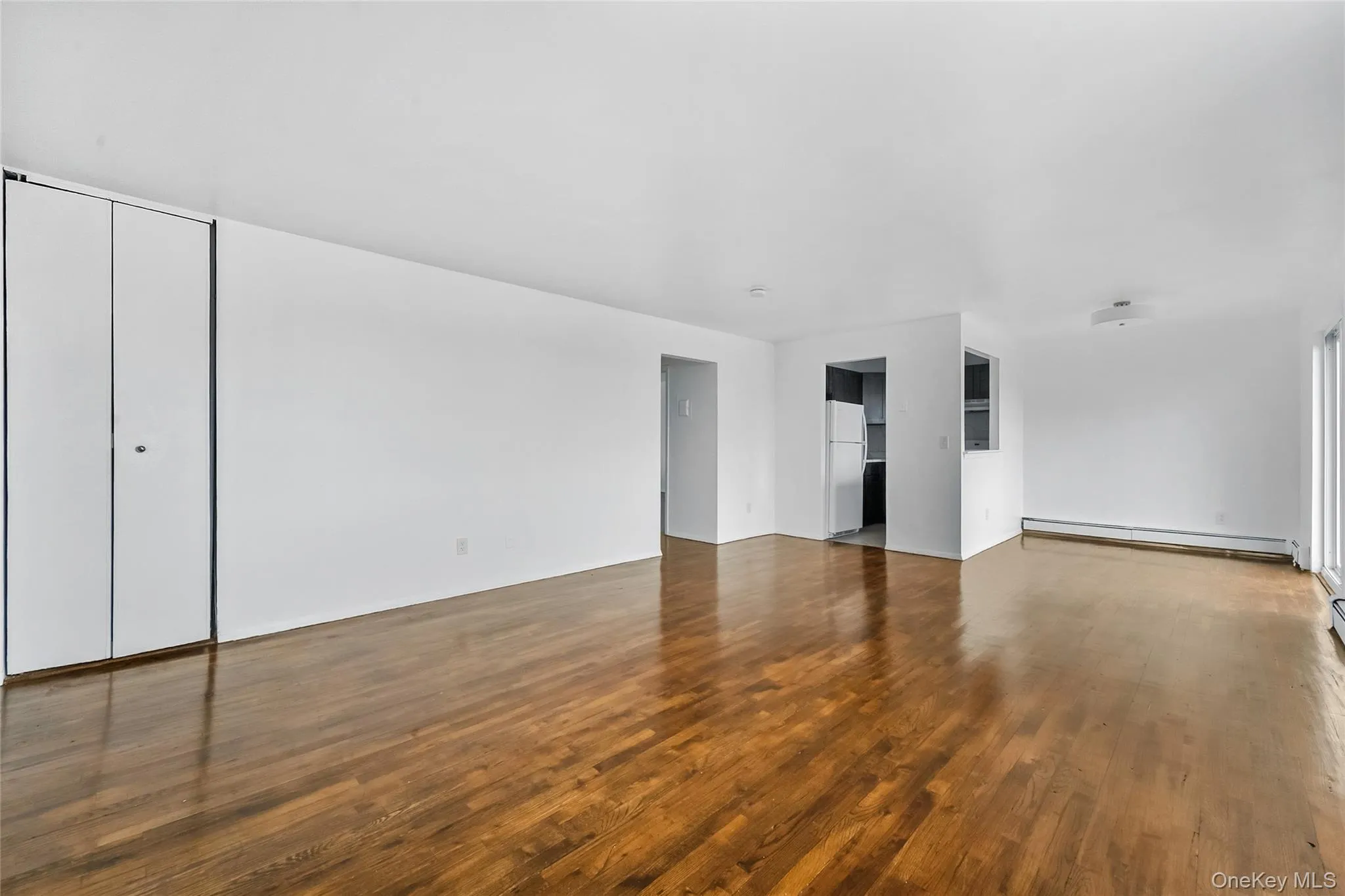 Unfurnished living room featuring dark wood-type flooring and baseboard heating Unfurnished living room featuring dark wood-type flooring and baseboard heating