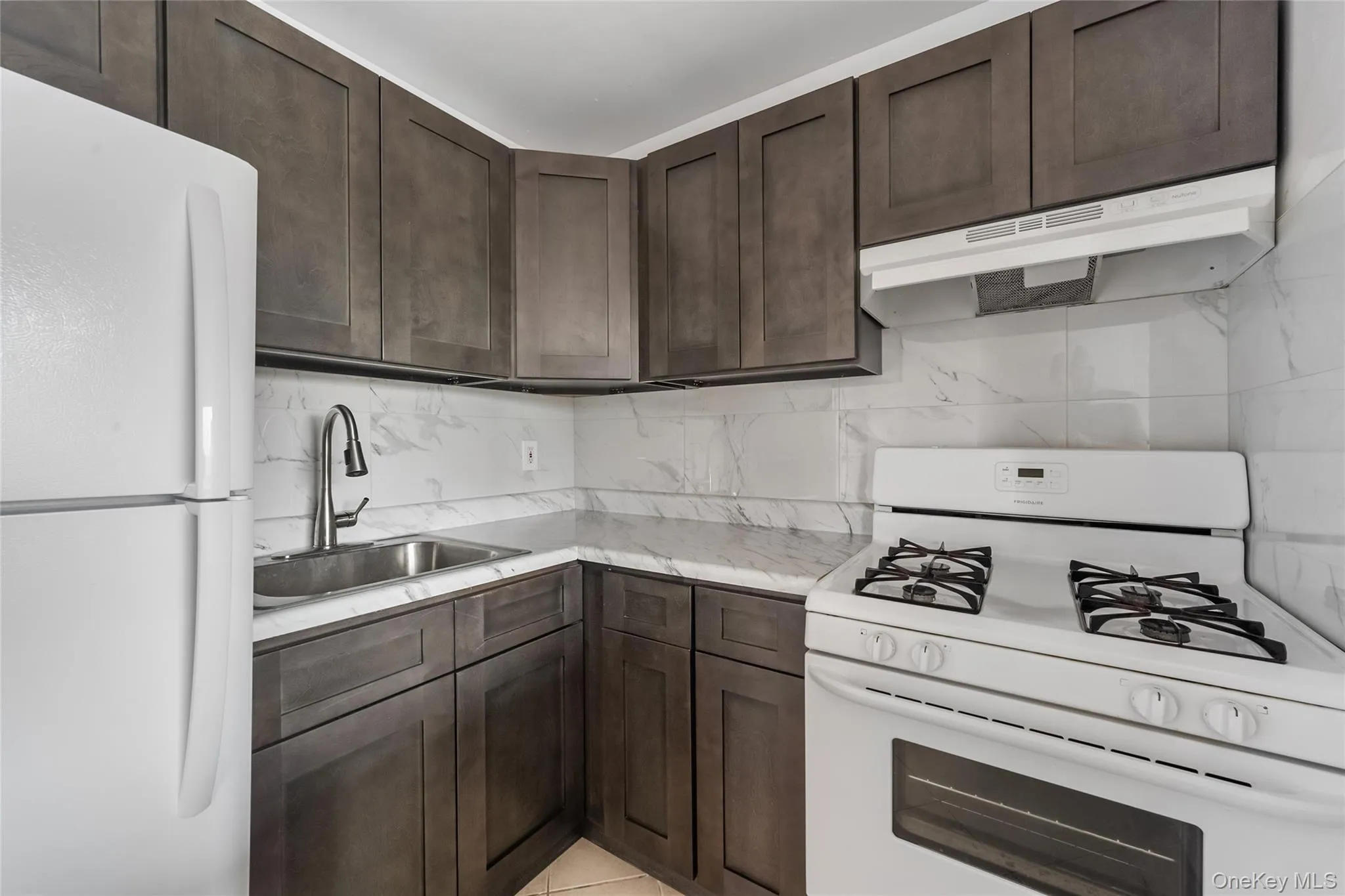 Kitchen with white appliances, dark brown cabinets, under cabinet range hood, and tasteful backsplash Kitchen with white appliances, dark brown cabinets, under cabinet range hood, and tasteful backsplash