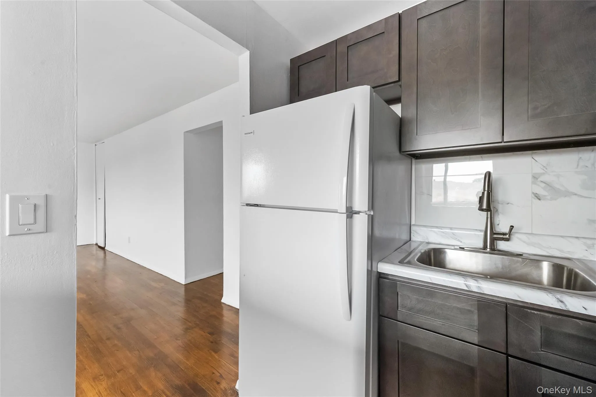 Kitchen featuring dark brown cabinets, freestanding refrigerator, dark wood-type flooring, and light countertops Kitchen featuring dark brown cabinets, freestanding refrigerator, dark wood-type flooring, and light countertops