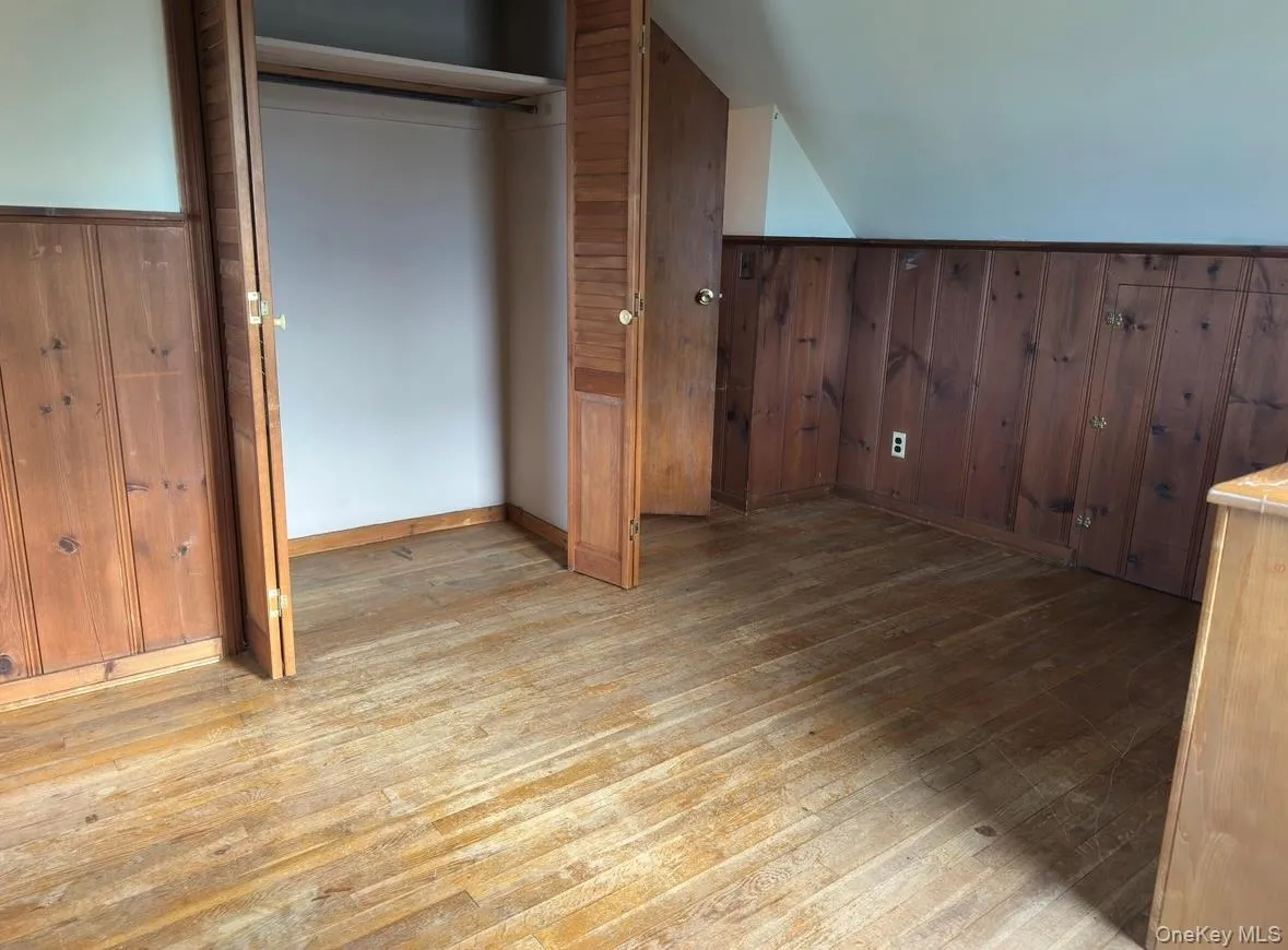 Bedroom with dark wood-style flooring, wainscoting, lofted ceiling, and wood walls Bedroom with dark wood-style flooring, wainscoting, lofted ceiling, and wood walls