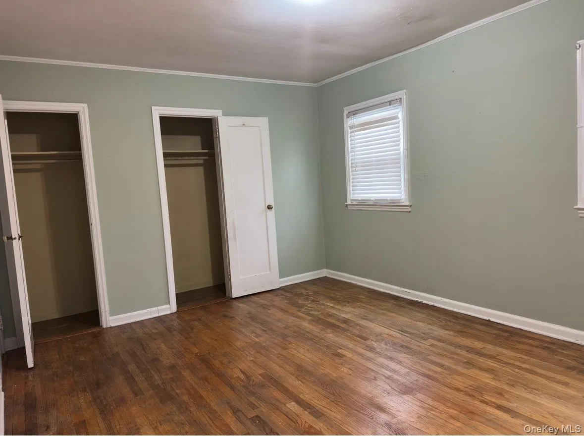 Unfurnished bedroom with two closets, dark wood finished floors, and crown molding Unfurnished bedroom with two closets, dark wood finished floors, and crown molding