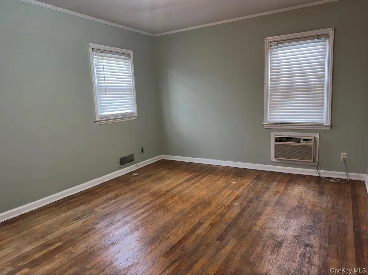 Spare room with crown molding, dark wood-style flooring, and a wall mounted air conditioner Spare room with crown molding, dark wood-style flooring, and a wall mounted air conditioner