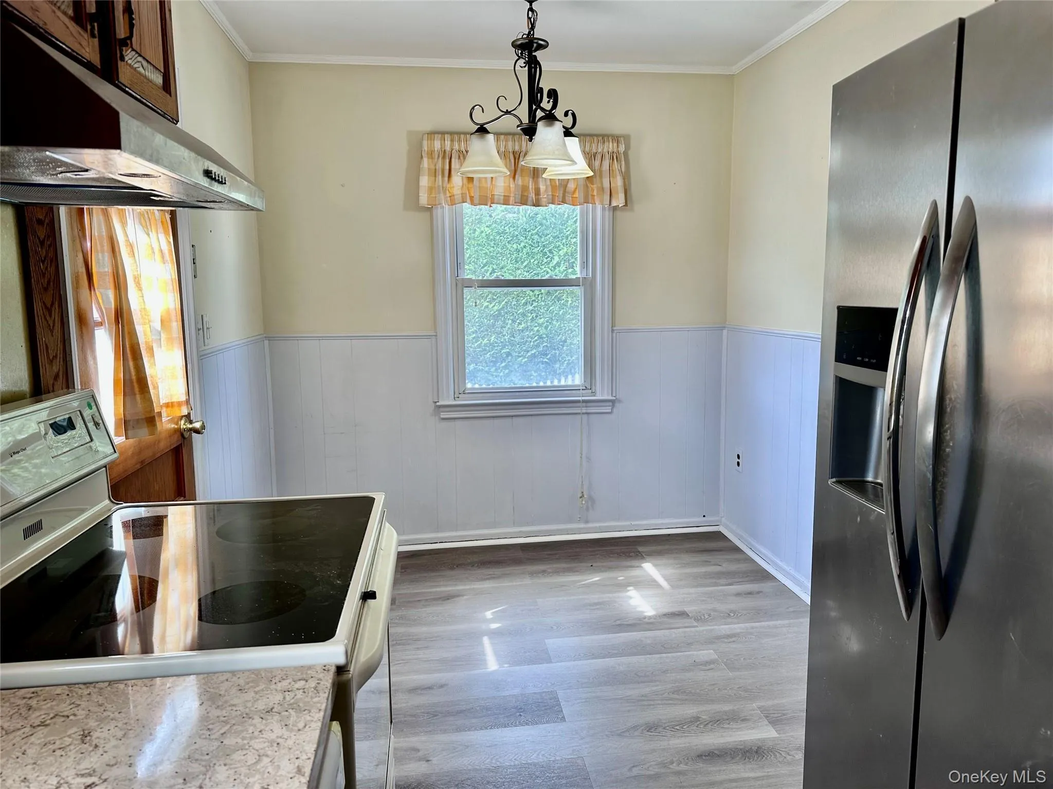 Kitchen with stainless steel refrigerator with ice dispenser, a wainscoted wall, white electric range, light wood-type flooring, and under cabinet range hood Kitchen with stainless steel refrigerator with ice dispenser, a wainscoted wall, white electric range, light wood-type flooring, and under cabinet range hood