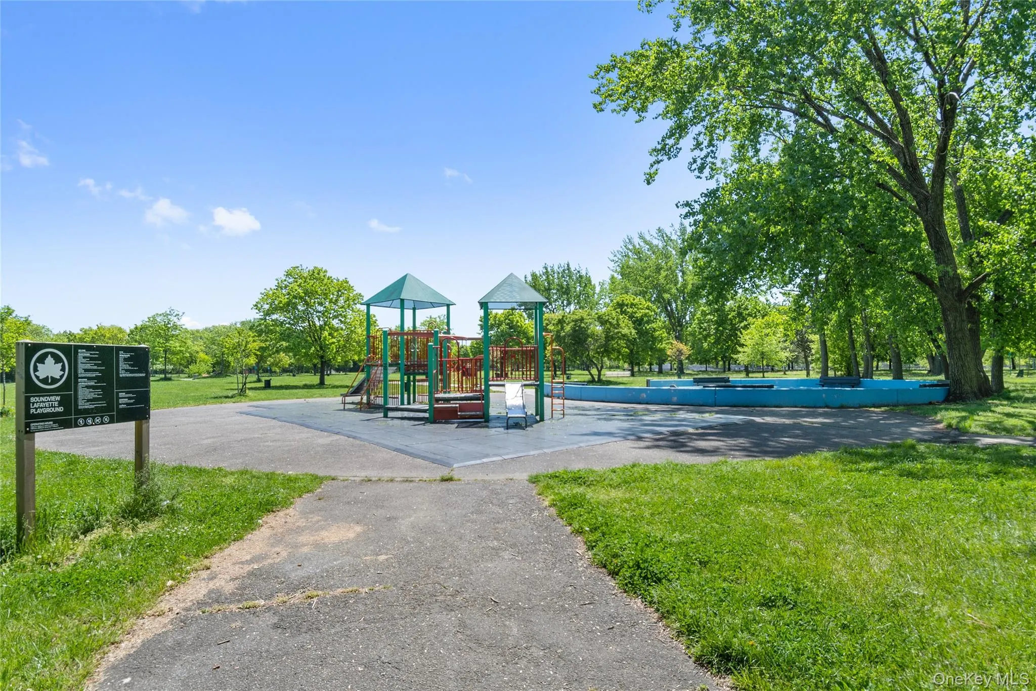 Outdoor playground with rubberized surfacing, adjacent green space, and mature trees Outdoor playground with rubberized surfacing, adjacent green space, and mature trees
