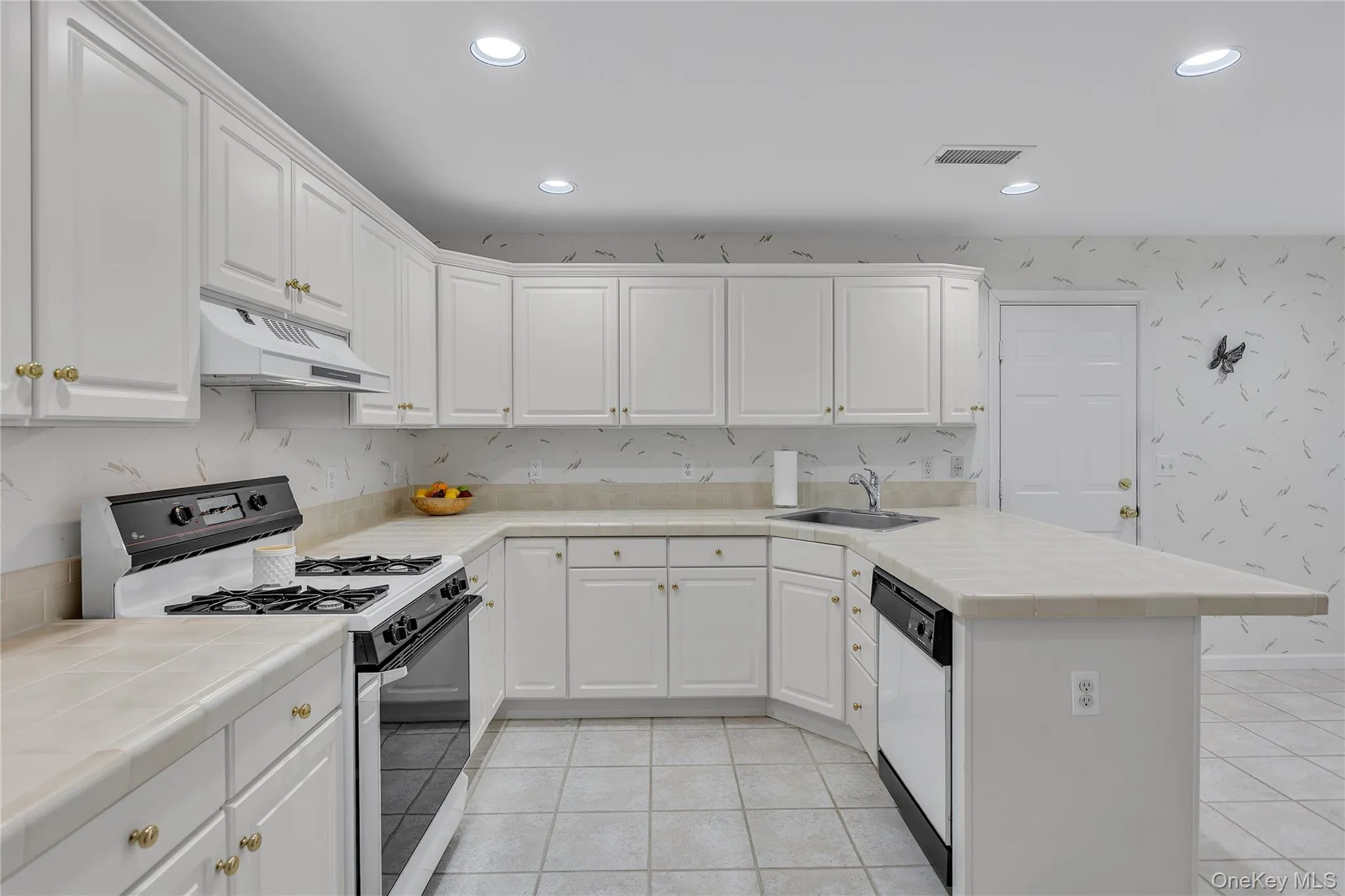 Kitchen featuring a tiled countertop, integrated dishwasher, white cabinetry, and recessed lighting. Access to the two-car attached garage. Kitchen featuring a tiled countertop, integrated dishwasher, white cabinetry, and recessed lighting. Access to the two-car attached garage.