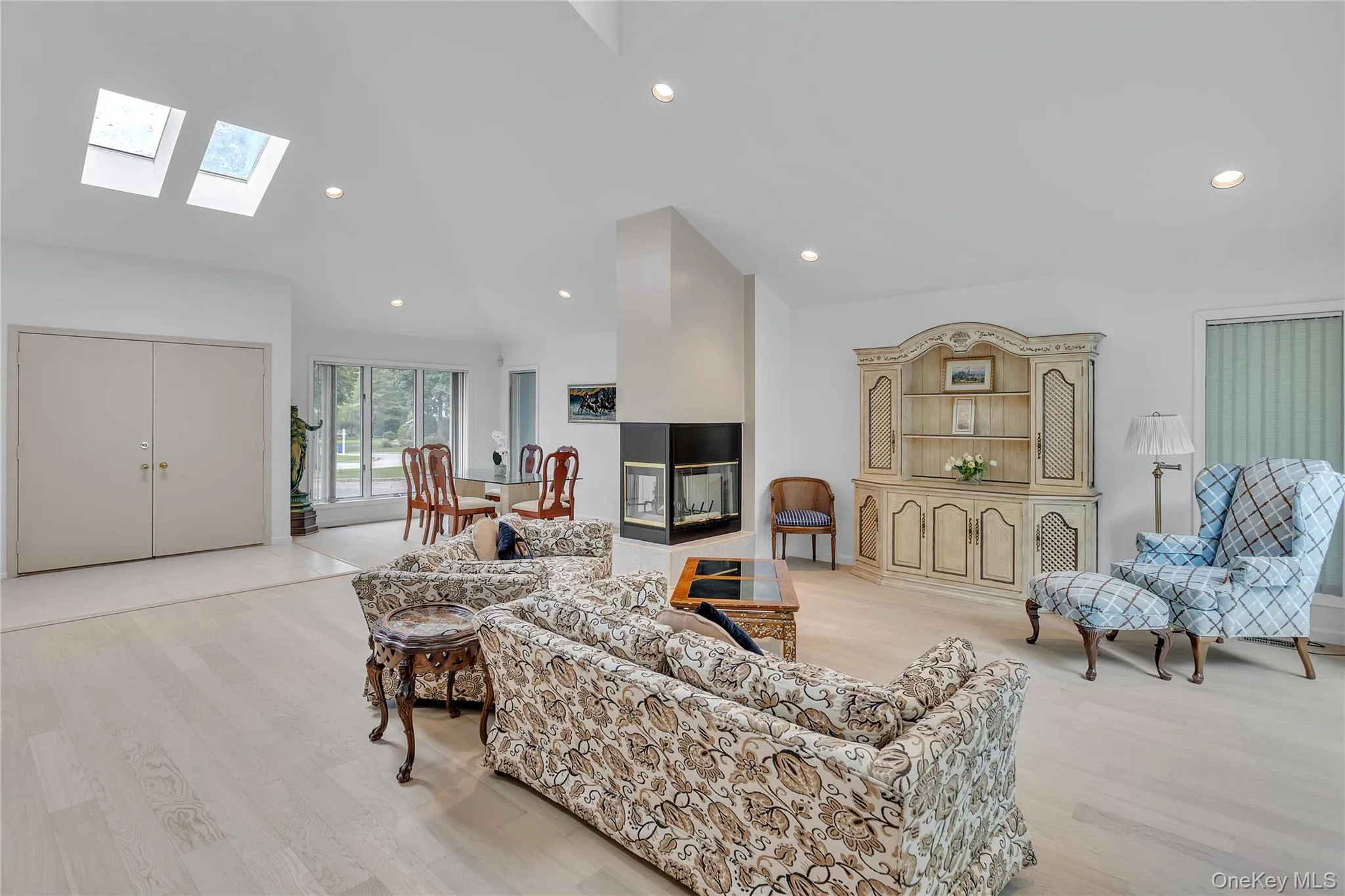 Vaulted ceiling interior featuring skylights, a multi-sided fireplace with a black surround, and a dining area with a large window. Vaulted ceiling interior featuring skylights, a multi-sided fireplace with a black surround, and a dining area with a large window.