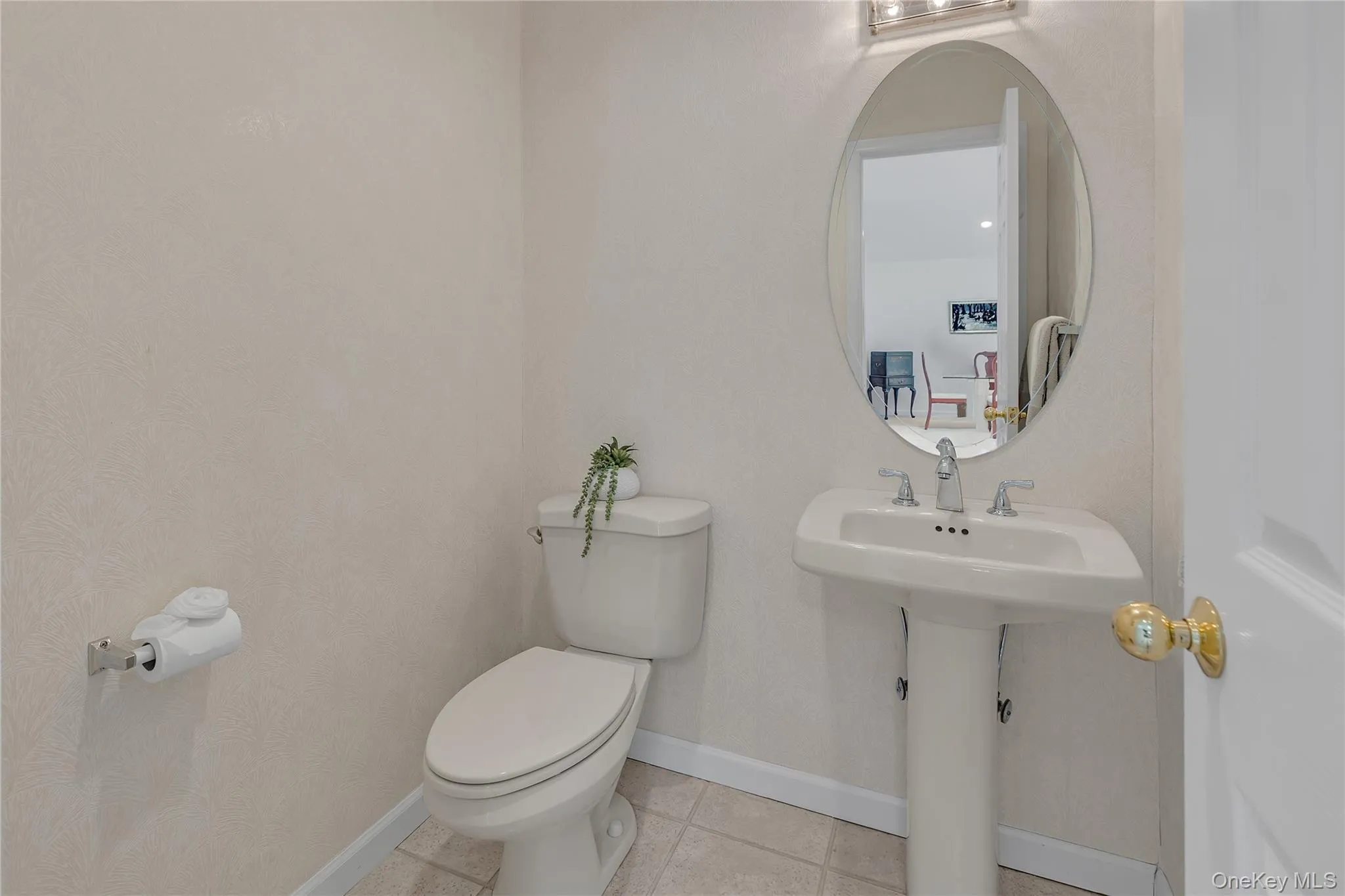 Pedestal sink with brushed nickel faucet, oval mirror, and three-light vanity fixture. Pedestal sink with brushed nickel faucet, oval mirror, and three-light vanity fixture.