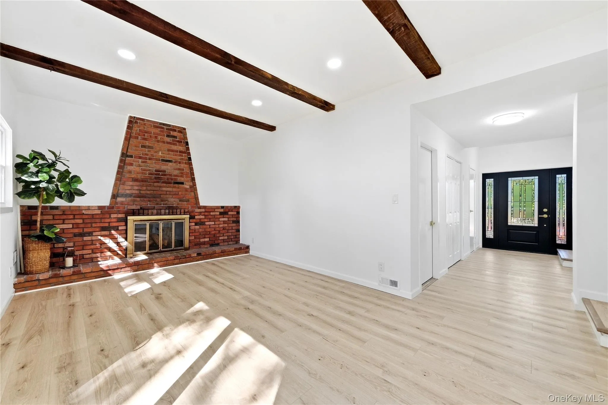 Exposed wood beams, recessed lighting, brick fireplace with metal insert, wood-finish flooring, and a dark-paneled entry door with decorative glass inserts Exposed wood beams, recessed lighting, brick fireplace with metal insert, wood-finish flooring, and a dark-paneled entry door with decorative glass inserts