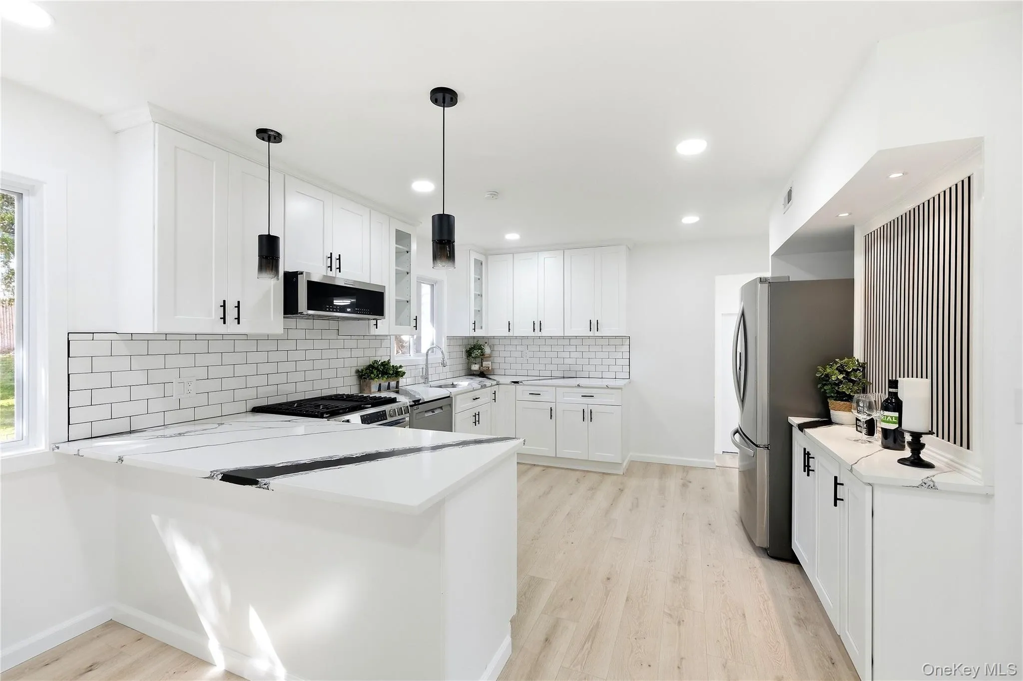 White shaker cabinetry with matte black hardware, white subway tile backsplash, stainless steel appliances, and wood-finish flooring White shaker cabinetry with matte black hardware, white subway tile backsplash, stainless steel appliances, and wood-finish flooring
