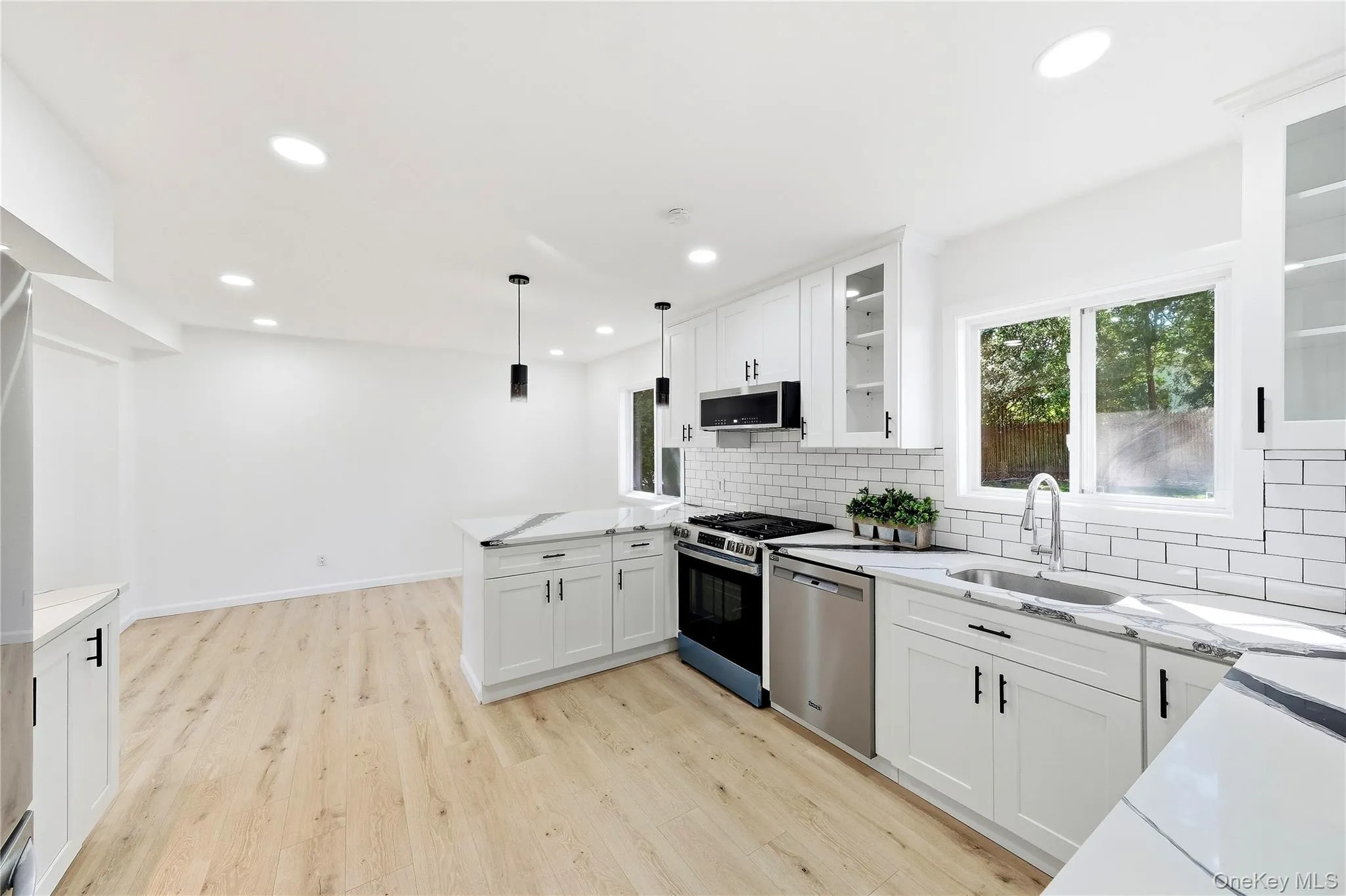 Modern kitchen featuring light wood-finish flooring, white shaker cabinetry, stainless steel appliances, a subway tile backsplash and dining area Modern kitchen featuring light wood-finish flooring, white shaker cabinetry, stainless steel appliances, a subway tile backsplash and dining area