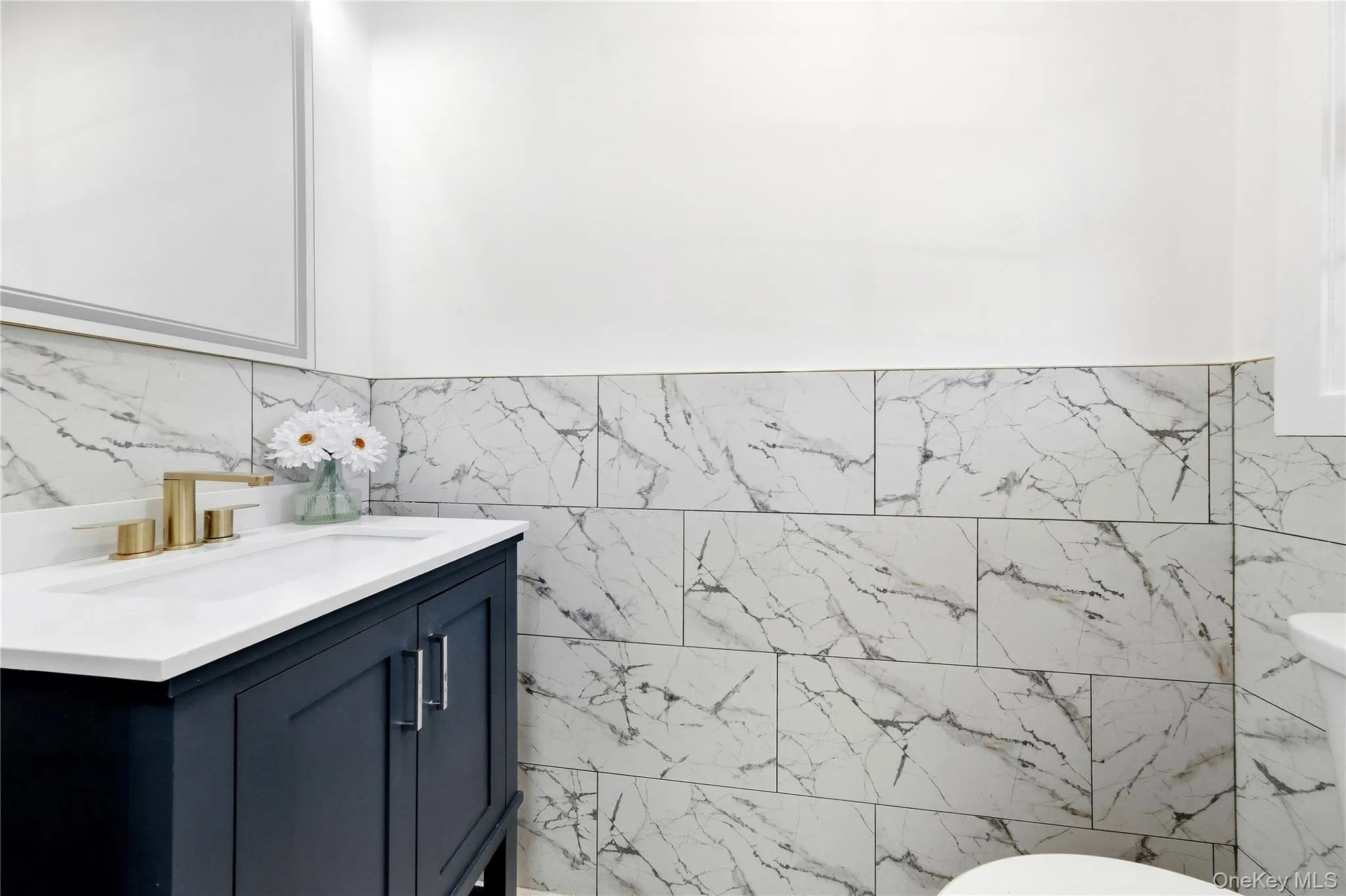 Dark-toned vanity with brushed gold-finish hardware, a white countertop, and an integrated rectangular sink and toilet. Dark-toned vanity with brushed gold-finish hardware, a white countertop, and an integrated rectangular sink and toilet.