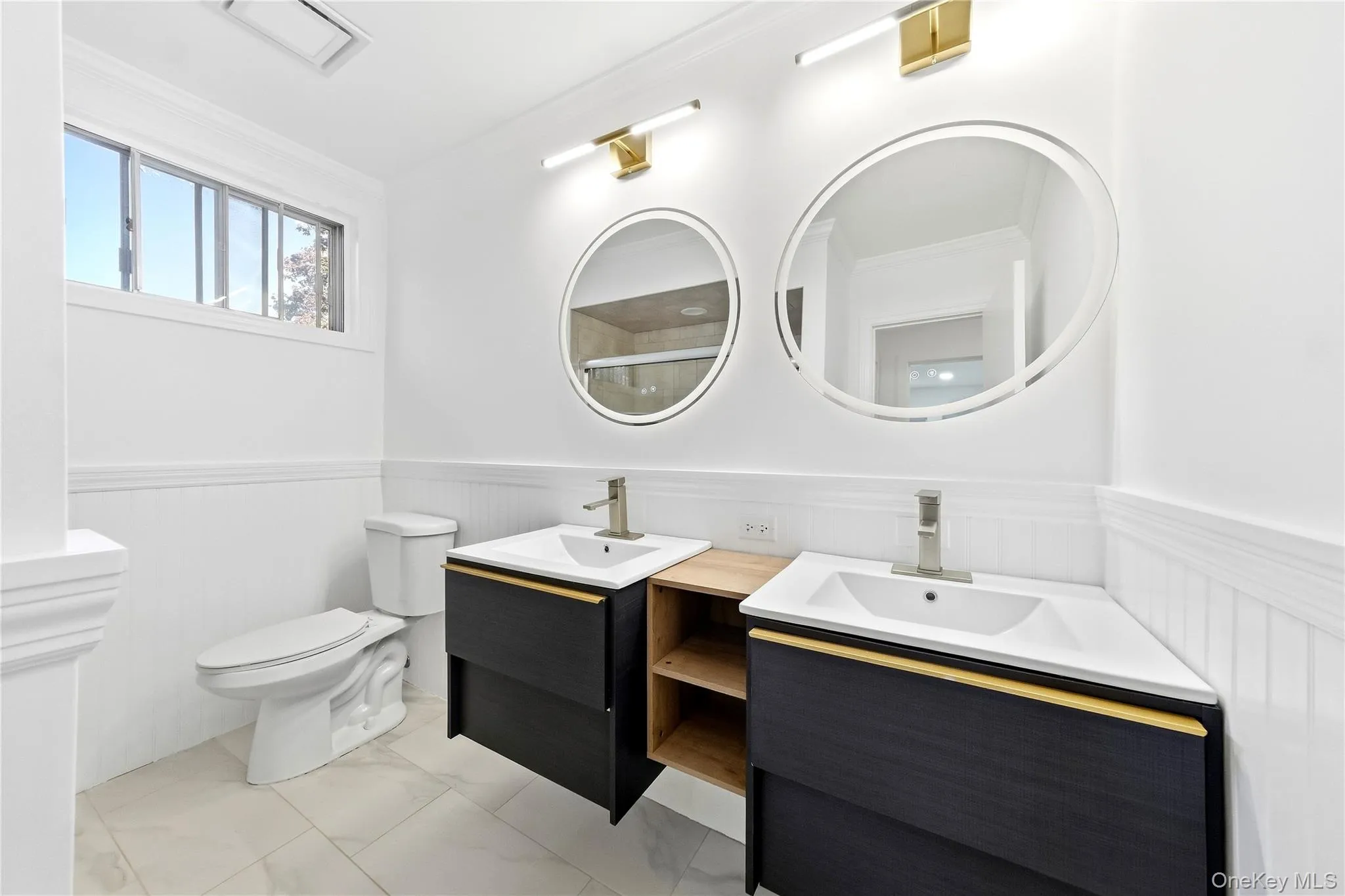 Dual floating vanities with integrated sinks, round back-lit mirrors, brushed gold fixtures and tub/shower combo Dual floating vanities with integrated sinks, round back-lit mirrors, brushed gold fixtures and tub/shower combo