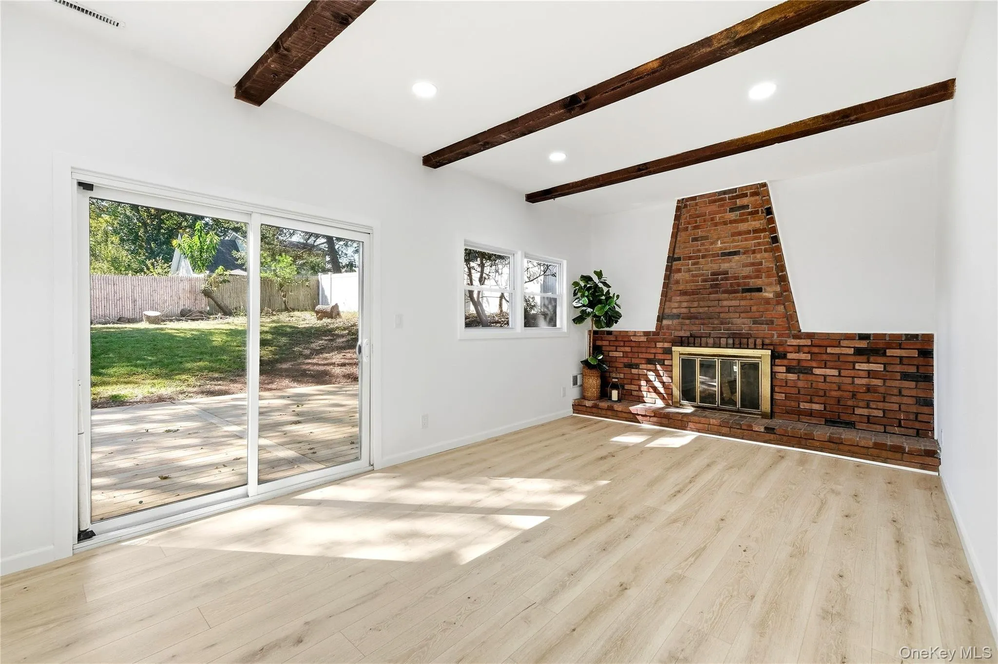 Wood-finish flooring, exposed ceiling beams, brick fireplace with metal insert, recessed lighting, and sliding glass door to a private outdoor space Wood-finish flooring, exposed ceiling beams, brick fireplace with metal insert, recessed lighting, and sliding glass door to a private outdoor space
