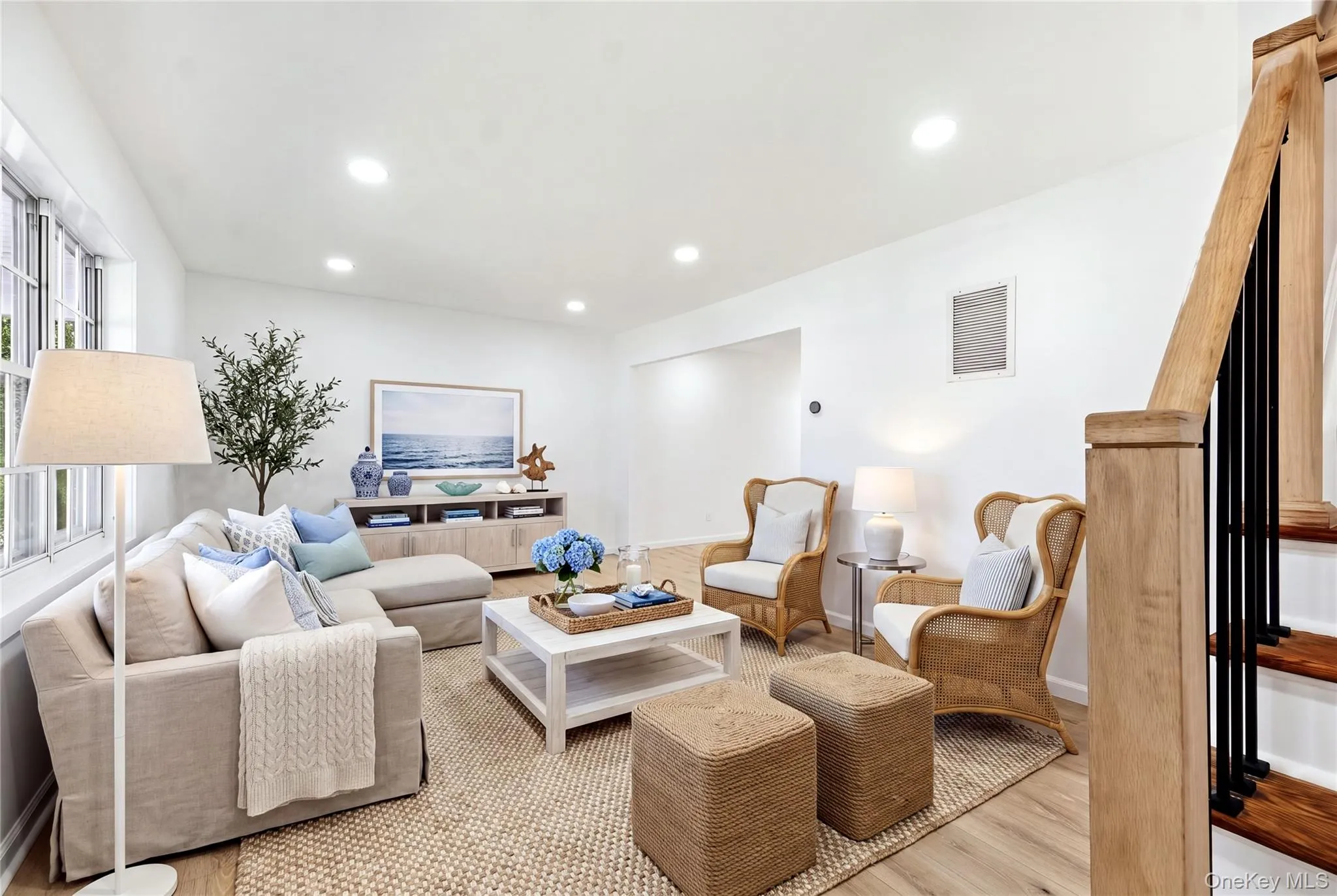 Bright living area featuring wood-finish flooring, recessed lighting, and a prominent staircase with wood handrail and black balusters Bright living area featuring wood-finish flooring, recessed lighting, and a prominent staircase with wood handrail and black balusters