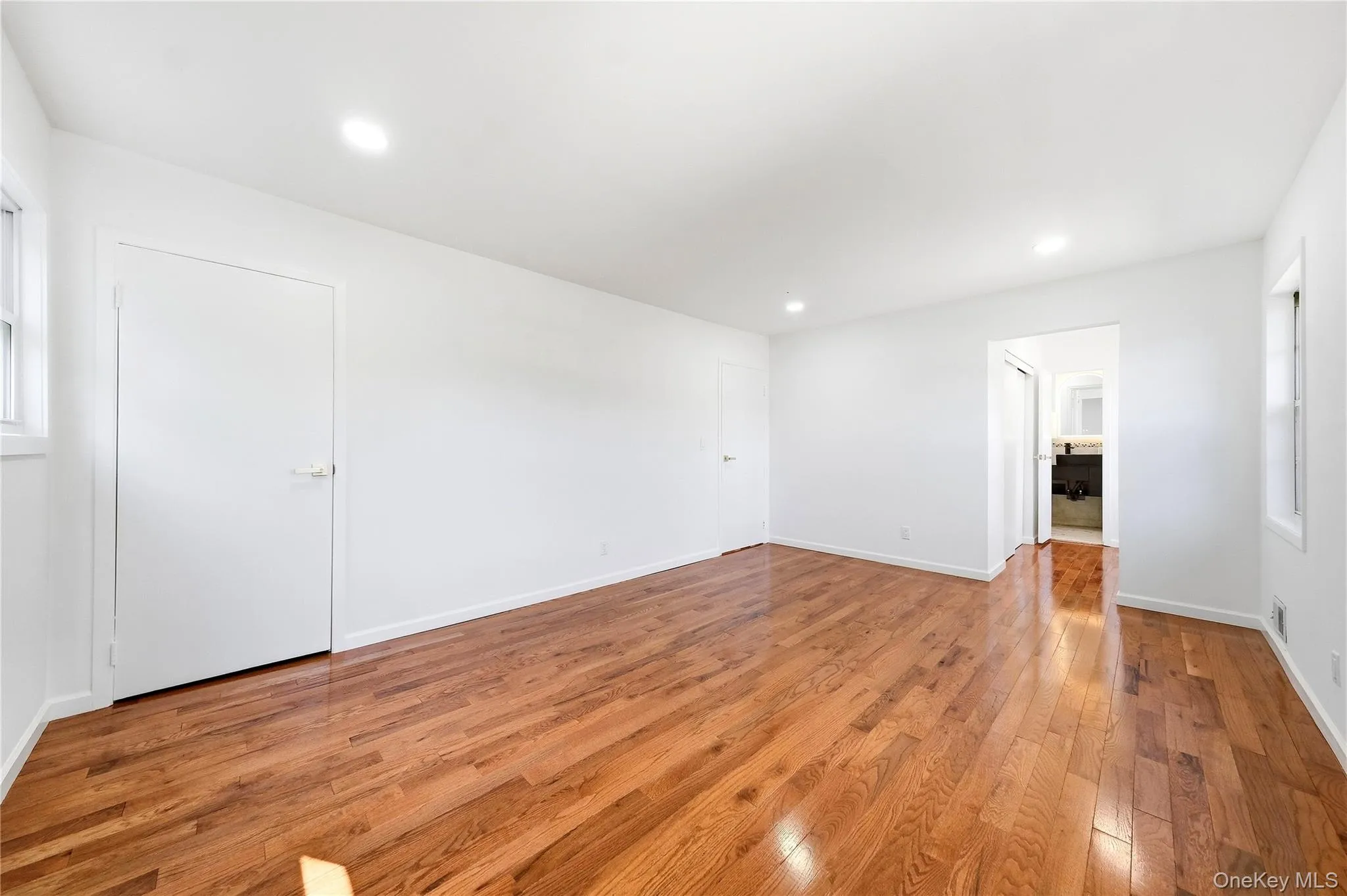 Expansive room featuring rich wood-finish flooring, recessed lighting, white walls, and multiple windows. Double closet leading to primary bathroom.Also featuring a separate closet in bedroom. Expansive room featuring rich wood-finish flooring, recessed lighting, white walls, and multiple windows. Double closet leading to primary bathroom.Also featuring a separate closet in bedroom.