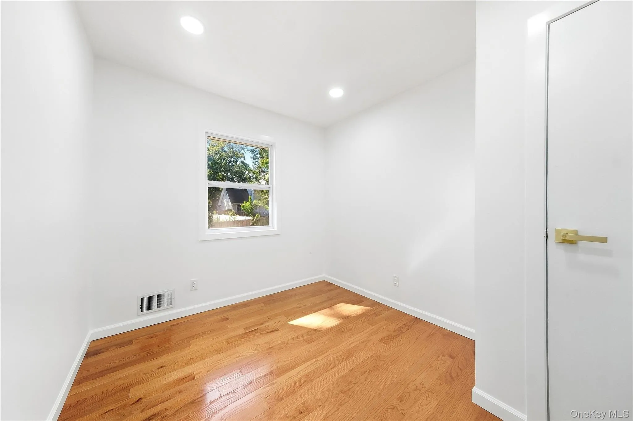 Hardwood flooring, recessed lighting, white interior walls, white trim, and a window with exterior scenery Hardwood flooring, recessed lighting, white interior walls, white trim, and a window with exterior scenery