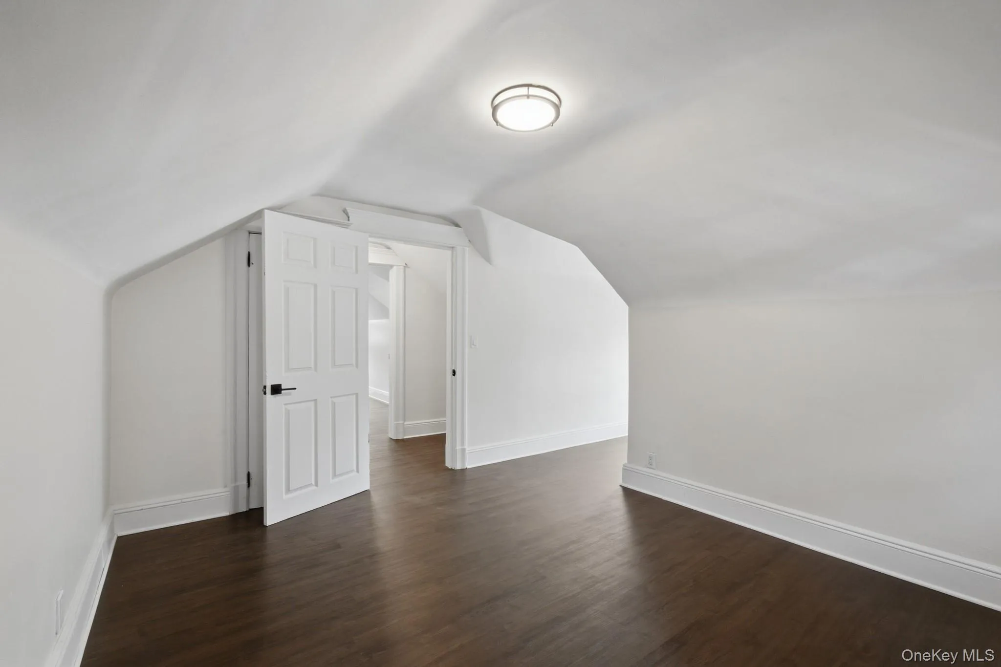 Spacious attic area featuring wood-finish flooring, white trim, and a flush mount ceiling fixture Spacious attic area featuring wood-finish flooring, white trim, and a flush mount ceiling fixture
