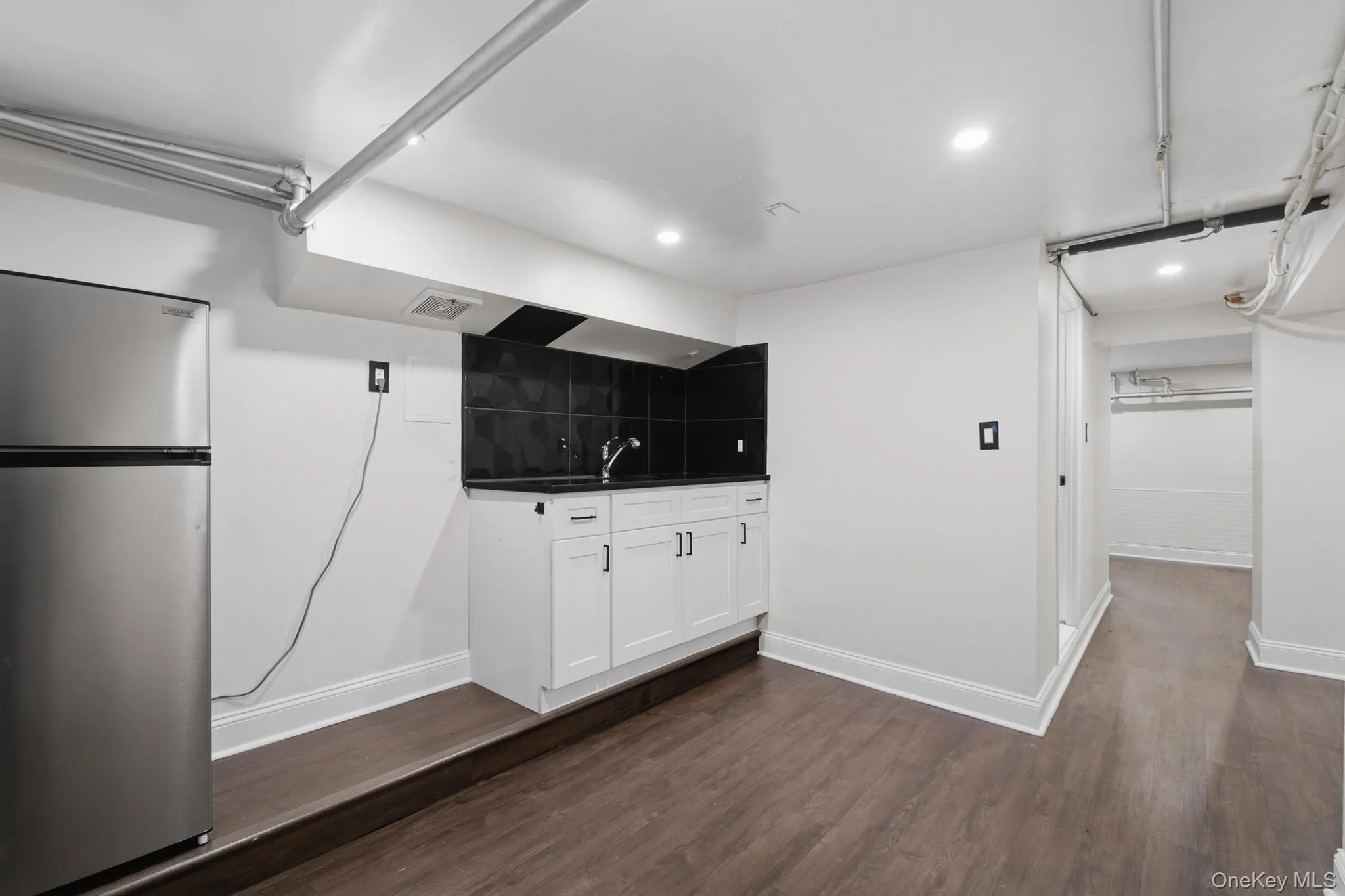 Stainless steel refrigerator, white cabinetry, dark countertop, and dark tile backsplash Stainless steel refrigerator, white cabinetry, dark countertop, and dark tile backsplash