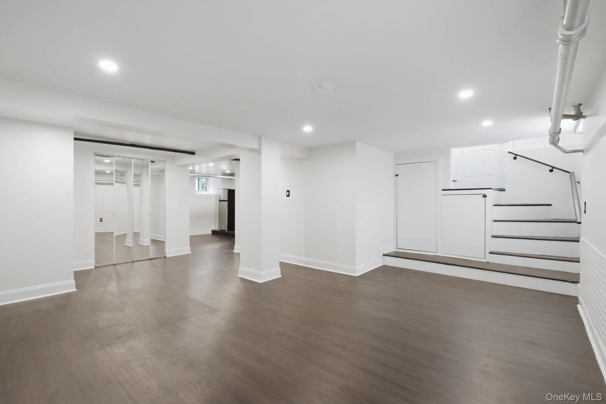Recessed lighting, wood-finish flooring, mirrored closet doors, white painted walls, and a black handrail on stairs Recessed lighting, wood-finish flooring, mirrored closet doors, white painted walls, and a black handrail on stairs