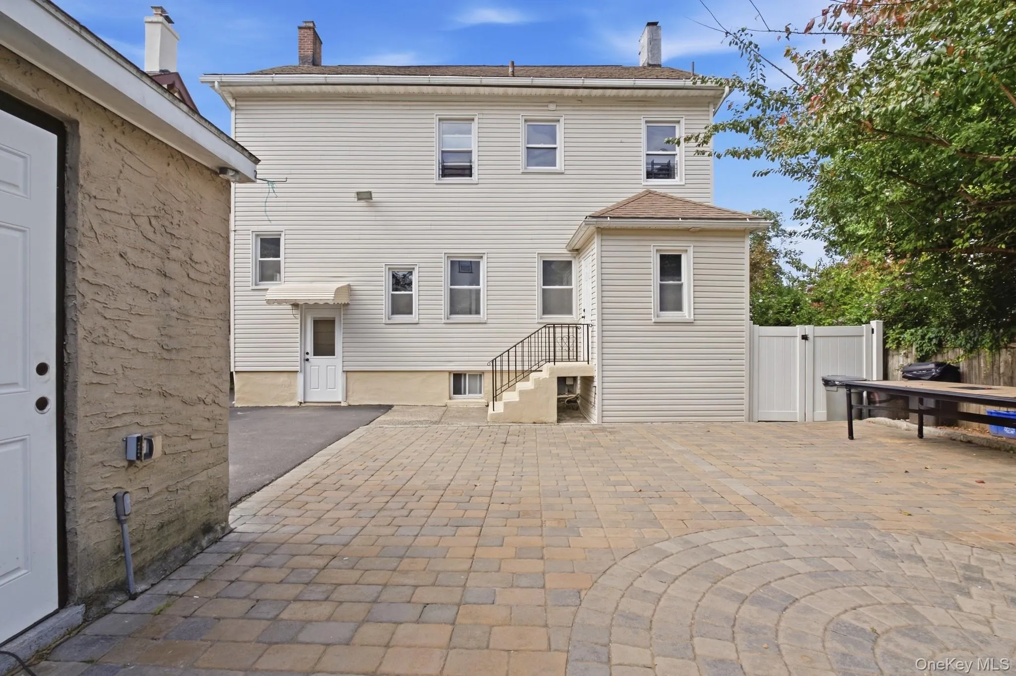 Expansive paver patio with a circular pattern, vinyl privacy fencing, rear entry access, and a secondary structure with stucco siding Expansive paver patio with a circular pattern, vinyl privacy fencing, rear entry access, and a secondary structure with stucco siding