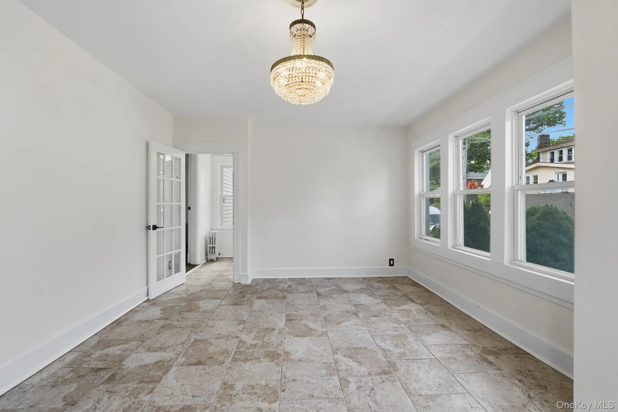 Warm neutral-toned floor tile throughout, bright recessed lighting, and a crystal chandelier Warm neutral-toned floor tile throughout, bright recessed lighting, and a crystal chandelier