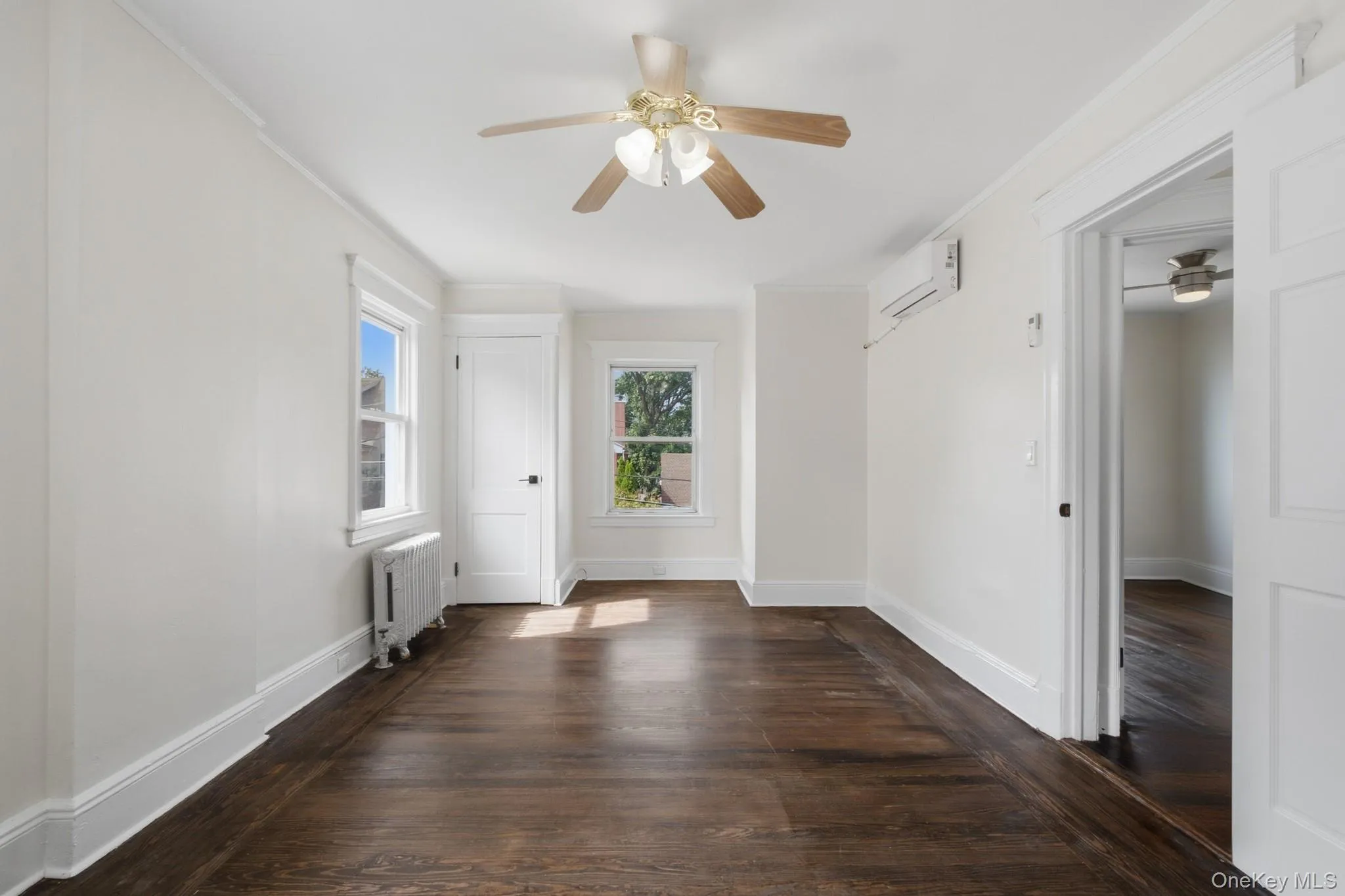 Wood-finish flooring, ceiling fan, white trim work, split-unit climate control, and a radiator Wood-finish flooring, ceiling fan, white trim work, split-unit climate control, and a radiator