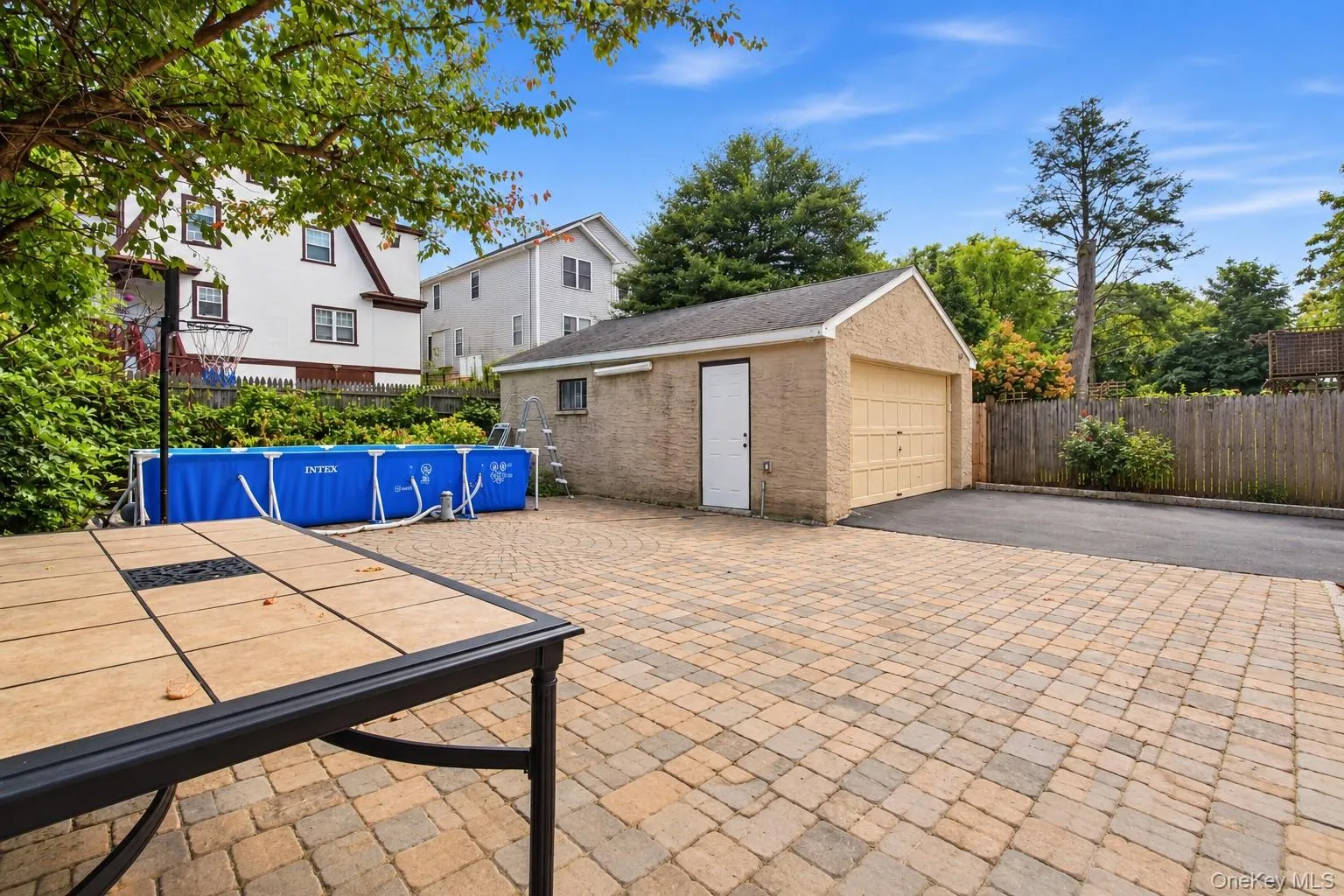 Paved patio area, detached garage with exterior door, paved driveway, and mature landscaping Paved patio area, detached garage with exterior door, paved driveway, and mature landscaping