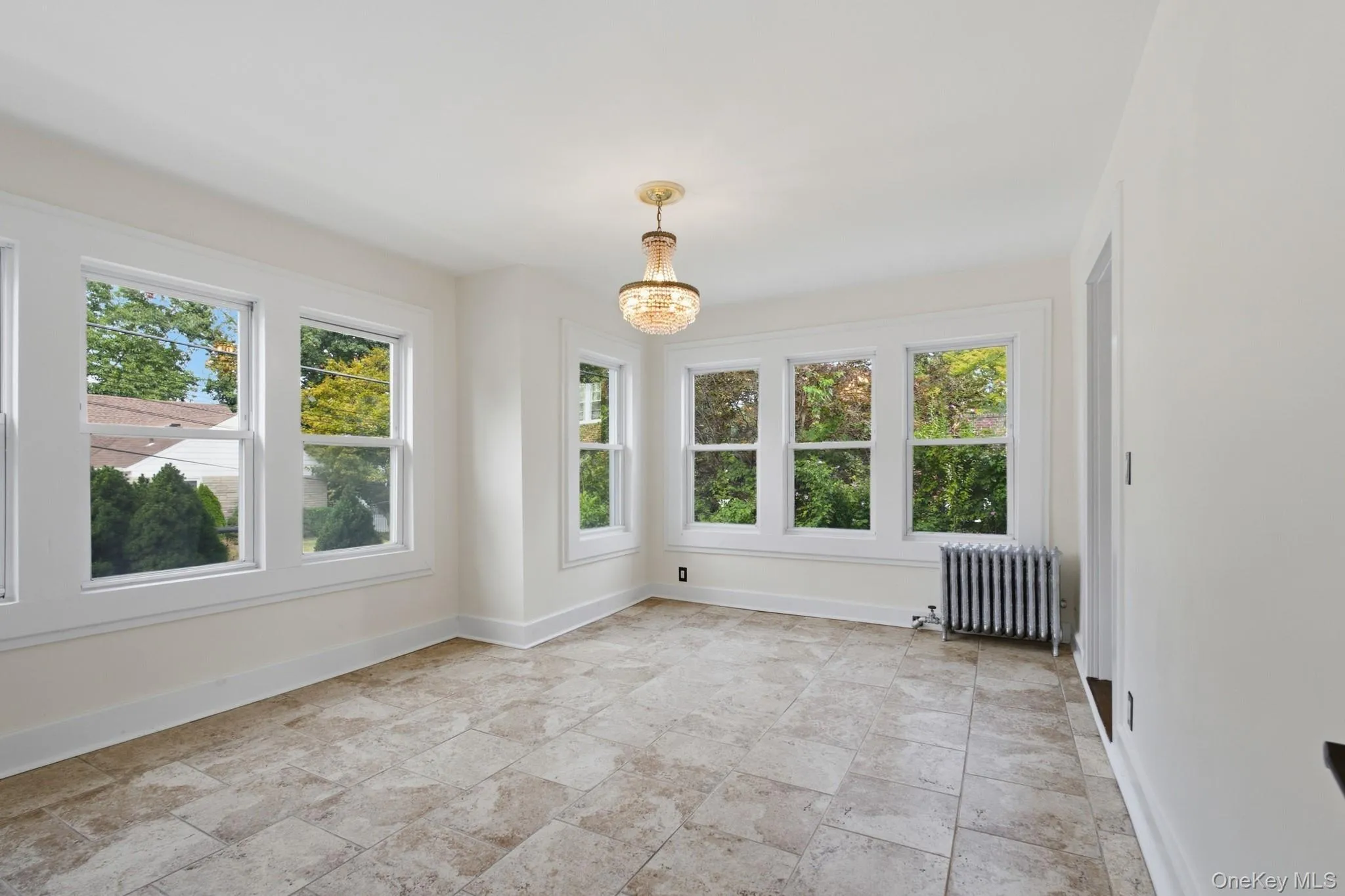Spacious room featuring multiple large windows, a decorative chandelier, and tile flooring Spacious room featuring multiple large windows, a decorative chandelier, and tile flooring