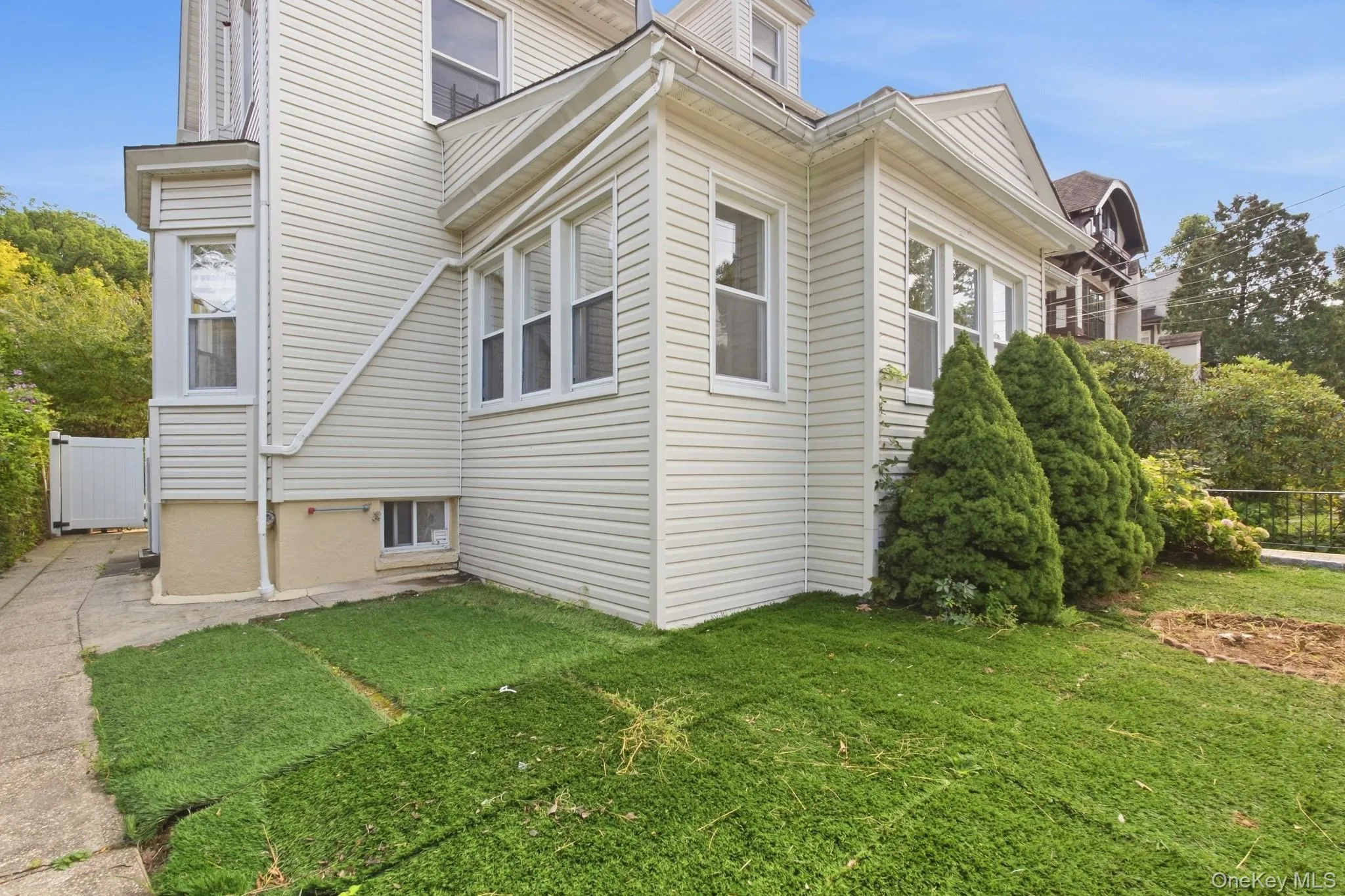 Exterior featuring light-colored siding, multiple windows, a foundation with a neutral finish, a concrete pathway, and established plantings Exterior featuring light-colored siding, multiple windows, a foundation with a neutral finish, a concrete pathway, and established plantings