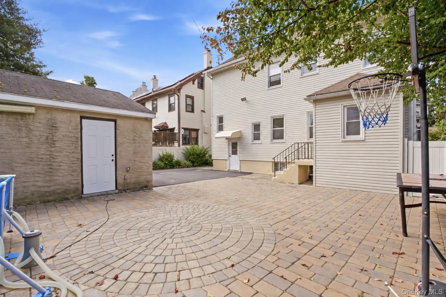 Expansive paver patio with a circular inlay, dedicated detached storage structure, and a rear entrance with exterior stairs Expansive paver patio with a circular inlay, dedicated detached storage structure, and a rear entrance with exterior stairs