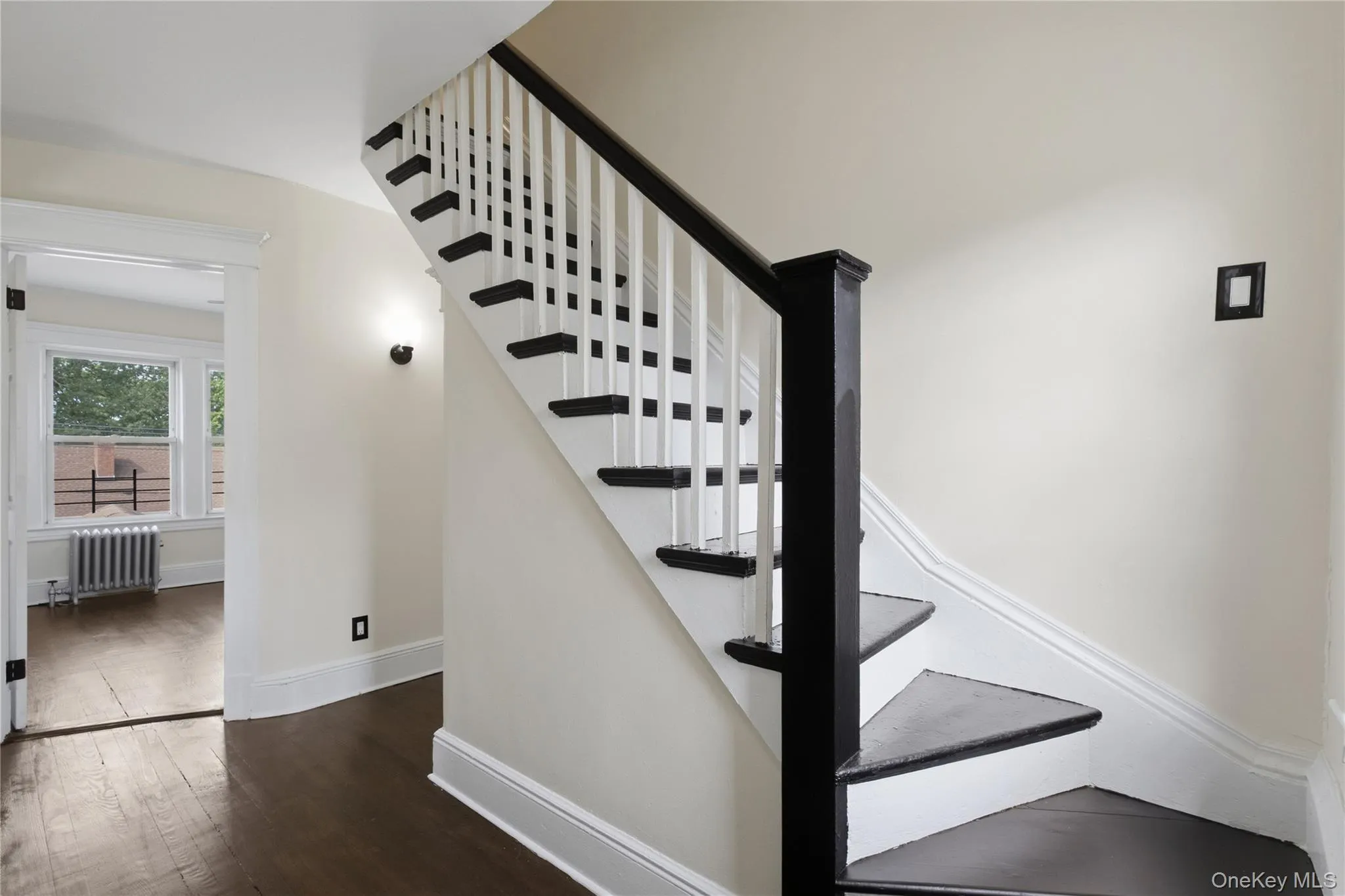 Hardwood flooring, painted staircase with dark treads and handrail, wall-mounted light fixture, white trim, and a window with natural light Hardwood flooring, painted staircase with dark treads and handrail, wall-mounted light fixture, white trim, and a window with natural light