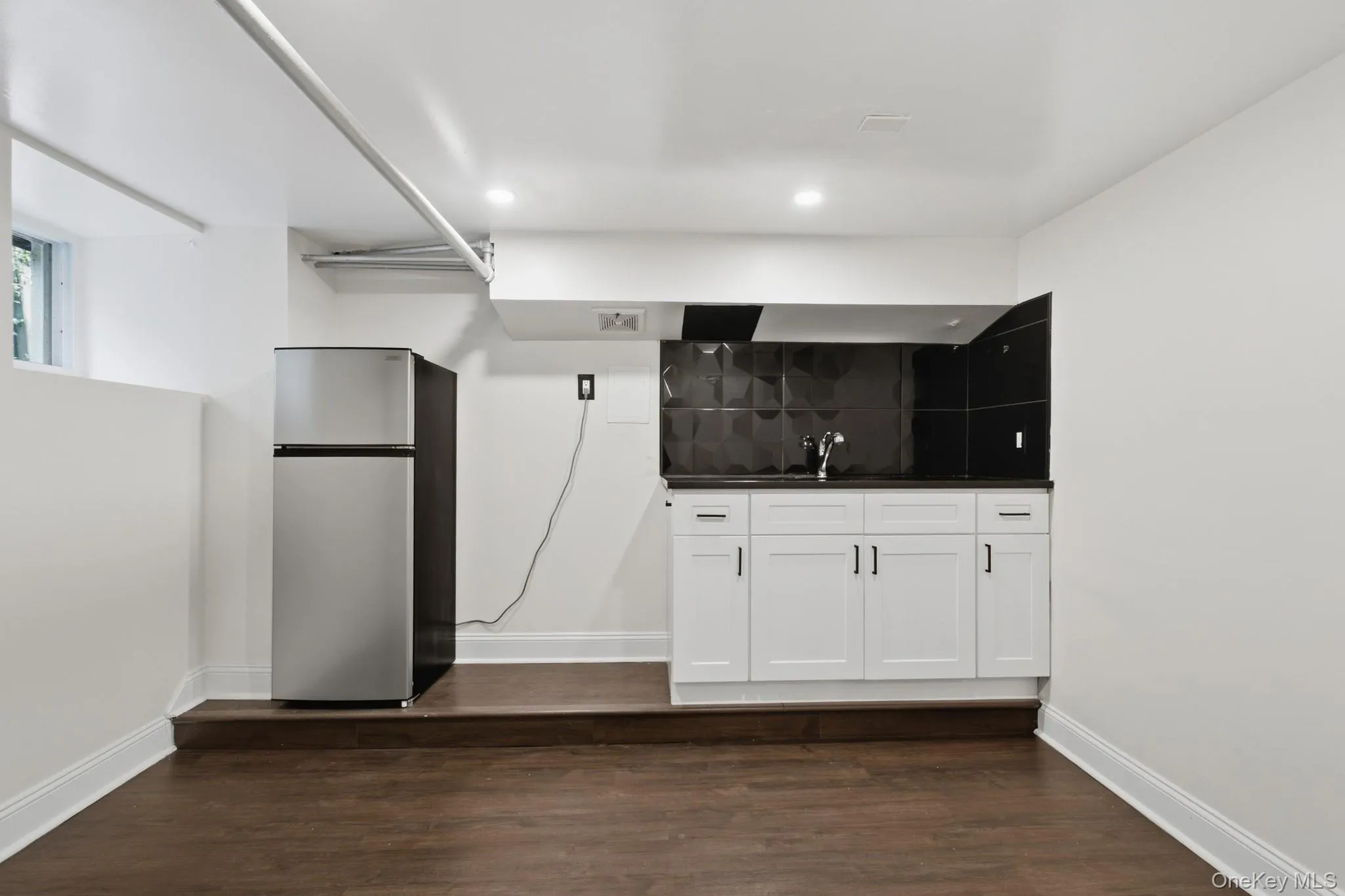 Compact kitchen area featuring white cabinetry, dark countertops, and a black patterned backsplash Compact kitchen area featuring white cabinetry, dark countertops, and a black patterned backsplash