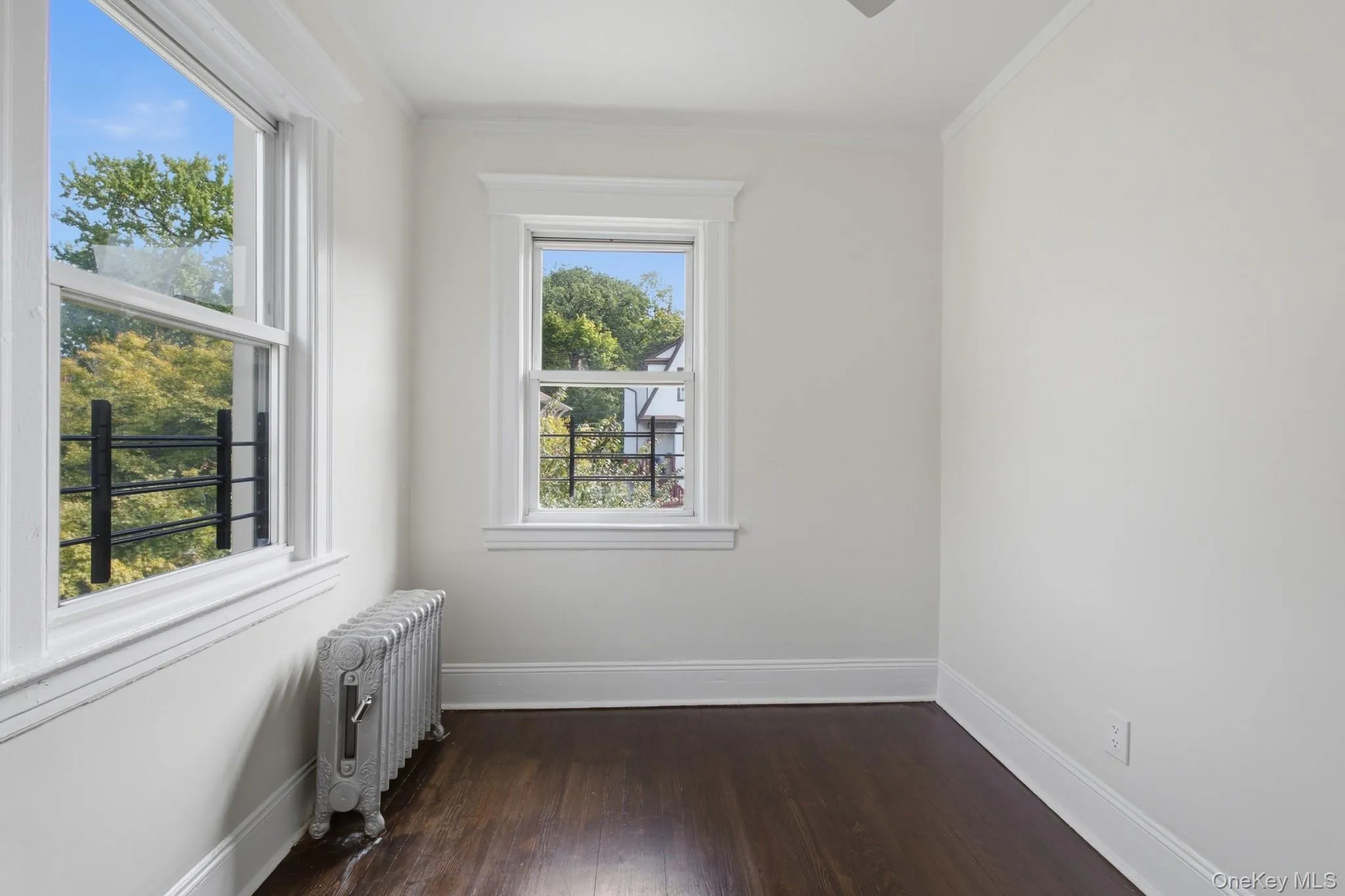 Hardwood flooring, painted white walls, two windows with white trim, and a cast iron radiator Hardwood flooring, painted white walls, two windows with white trim, and a cast iron radiator