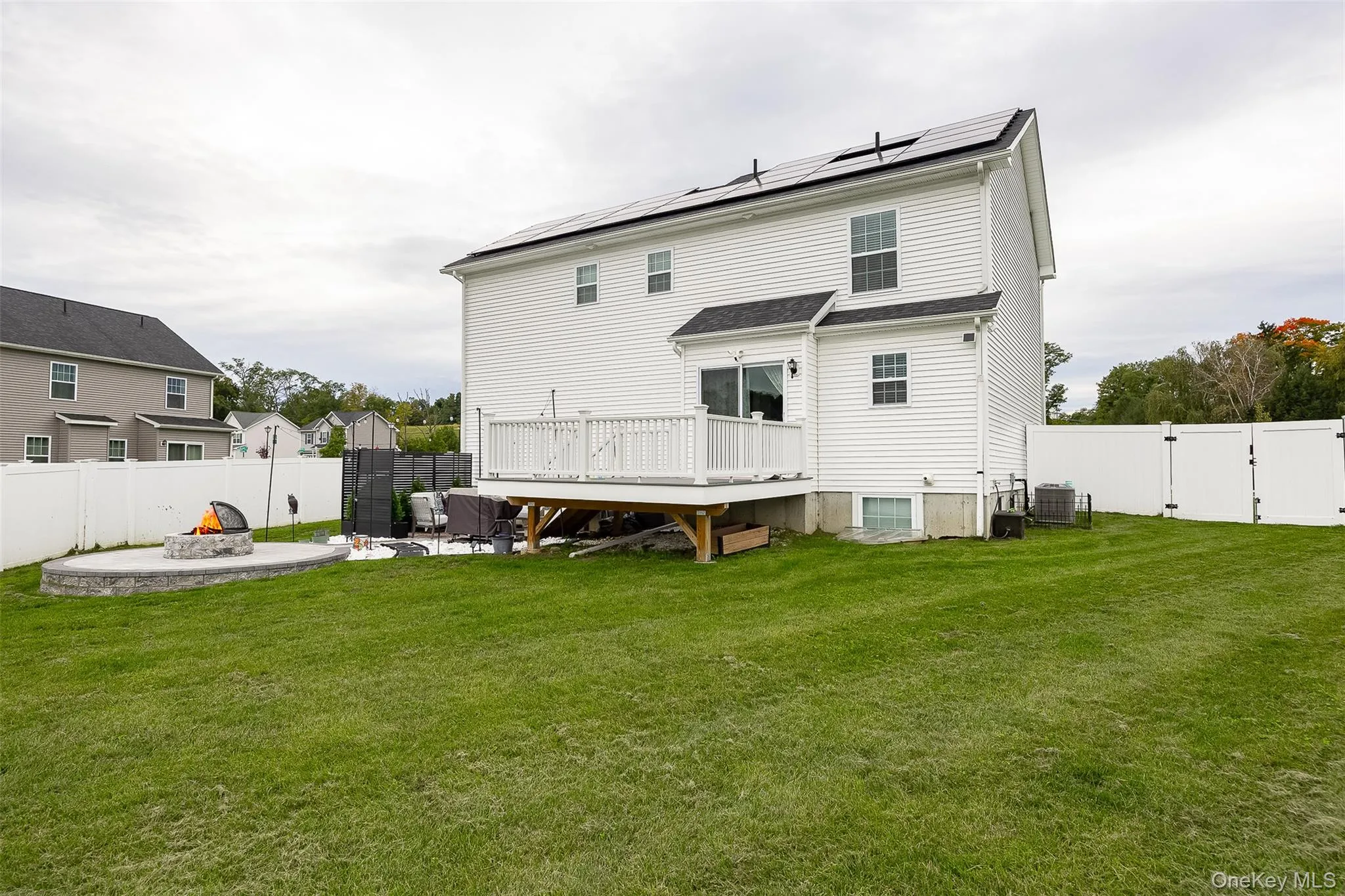 White vinyl siding exterior with solar panels, a private fenced yard, a large wood deck, and a circular stone fire pit White vinyl siding exterior with solar panels, a private fenced yard, a large wood deck, and a circular stone fire pit