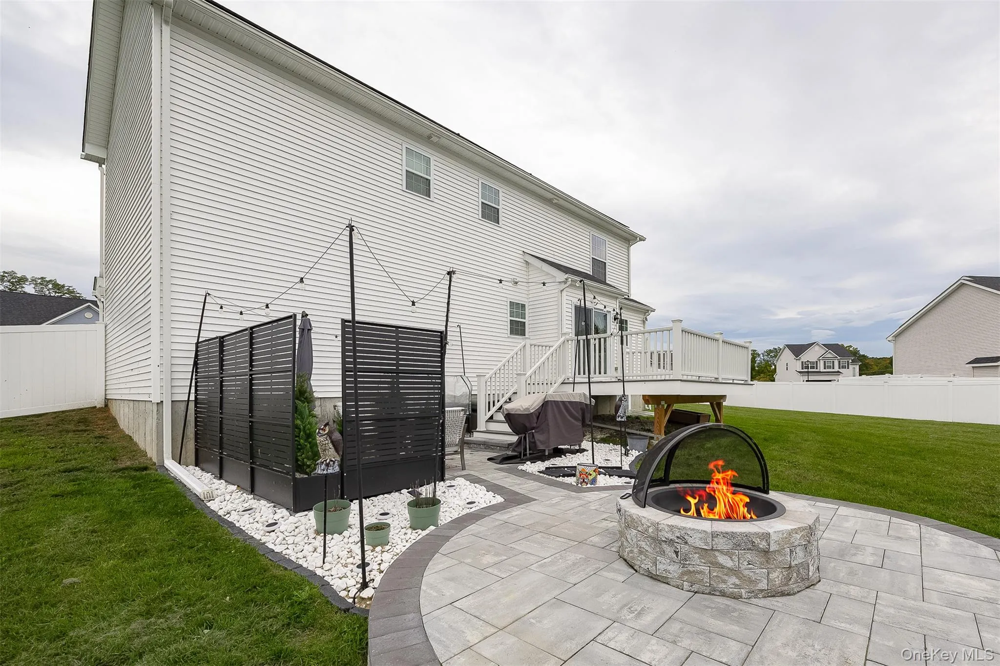 Backyard patio featuring a stone-finish fire pit, paver hardscaping, and a white privacy fence Backyard patio featuring a stone-finish fire pit, paver hardscaping, and a white privacy fence