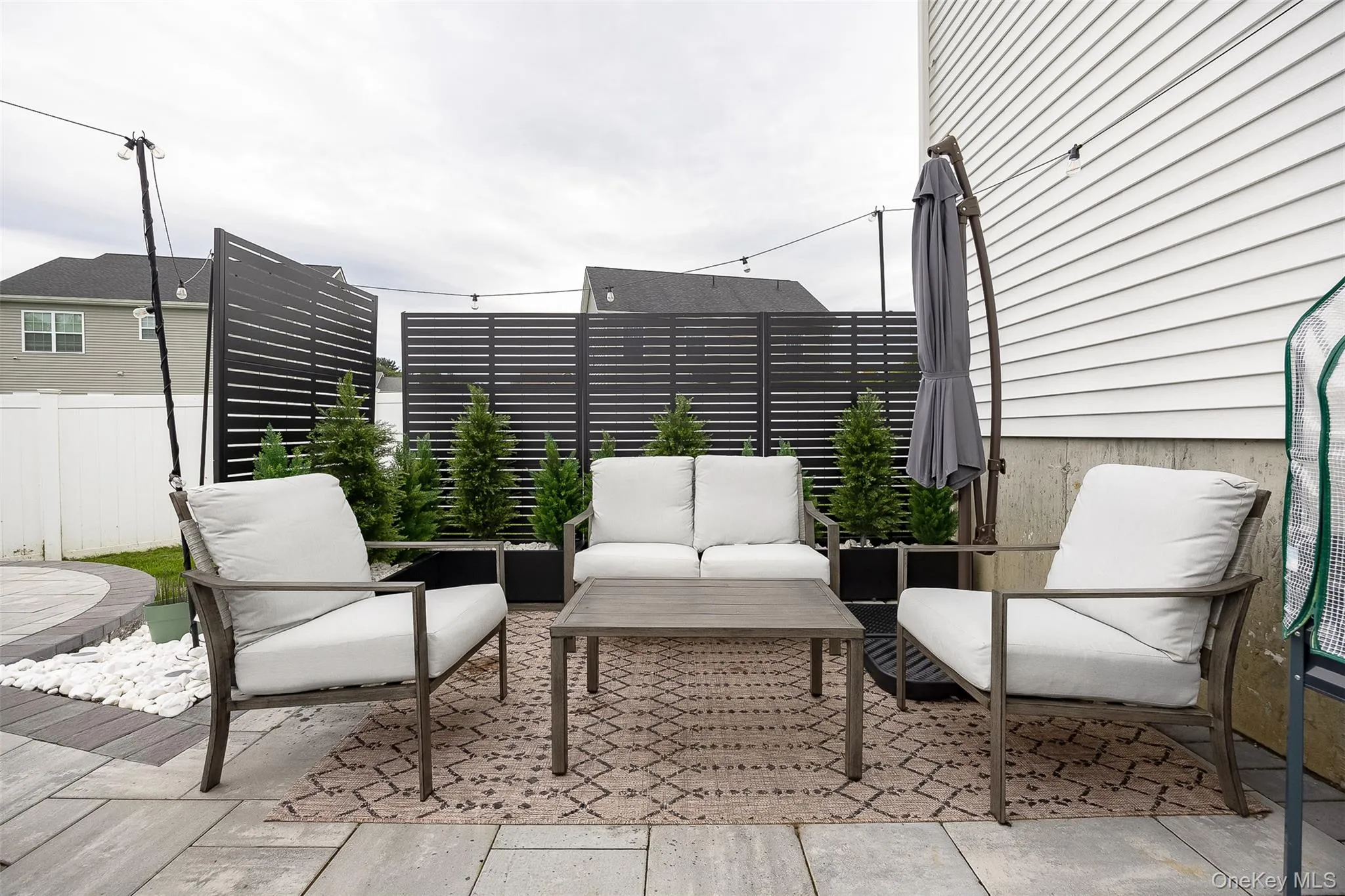 Paver patio with a circular inlay, white siding, and privacy screens Paver patio with a circular inlay, white siding, and privacy screens