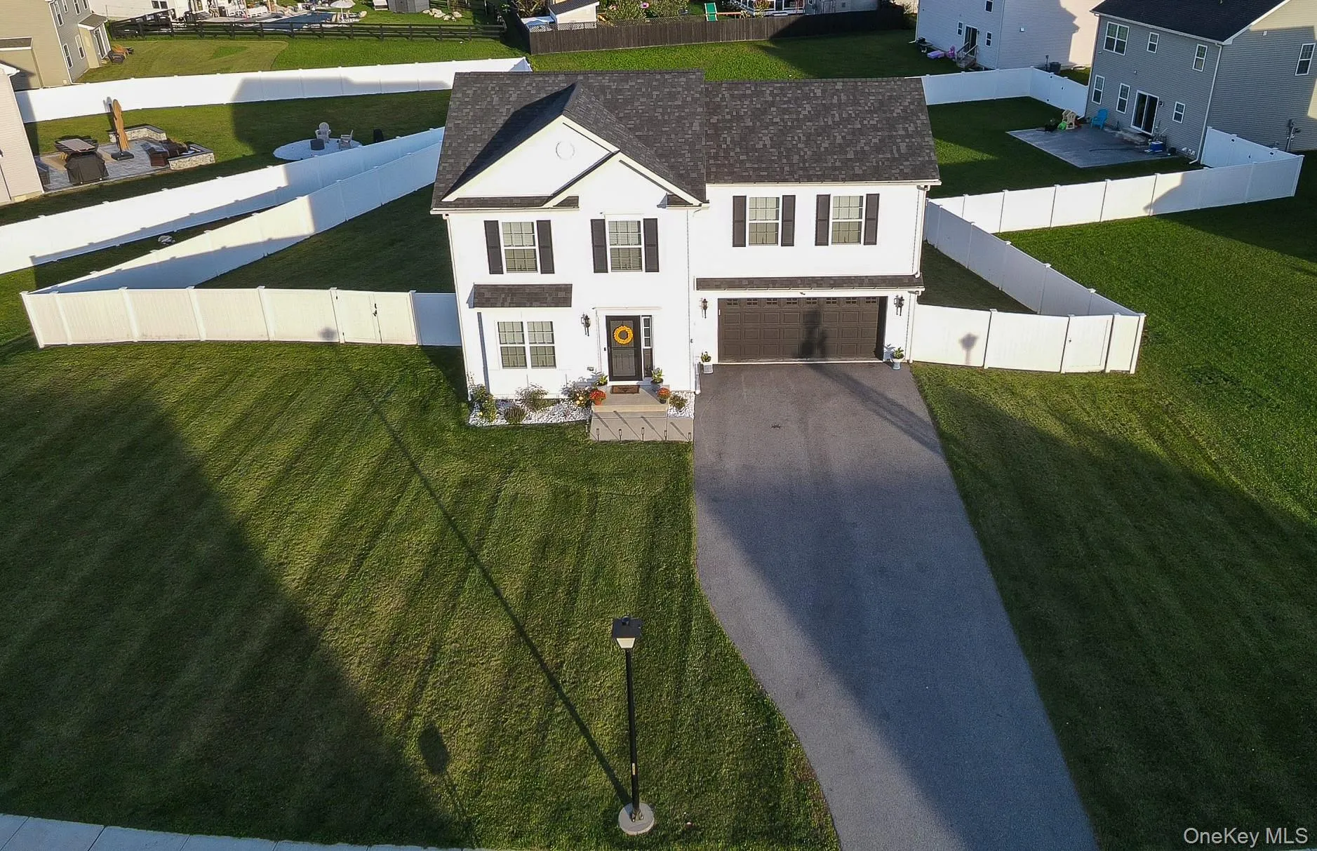 White two-story colonial-style residence with a dark shingle roof, attached two-car garage, extensive manicured lawn, and white privacy fencing White two-story colonial-style residence with a dark shingle roof, attached two-car garage, extensive manicured lawn, and white privacy fencing