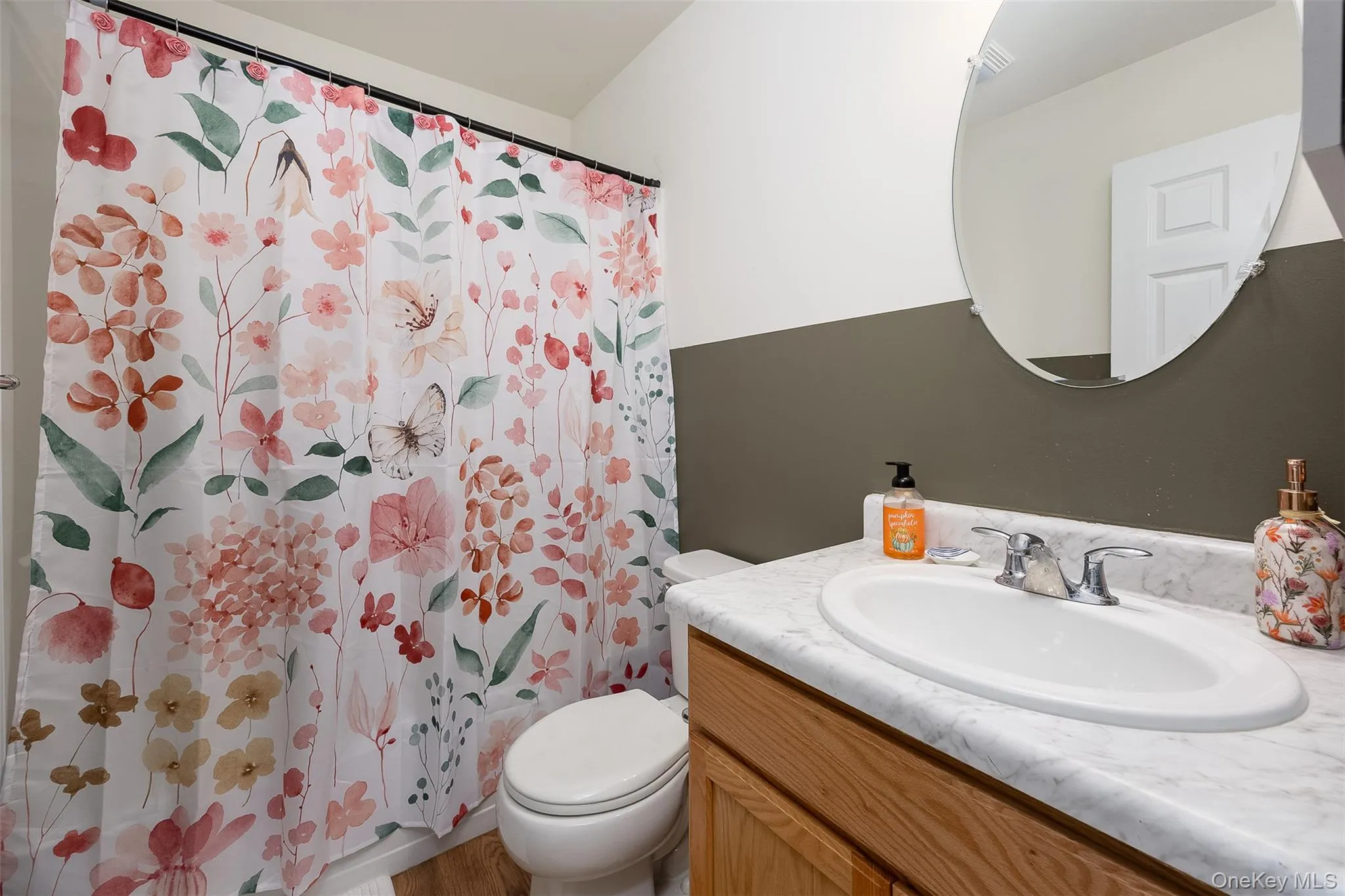 Bathroom featuring a wood-finish vanity with an integrated white sink, chrome faucet, and an oval wall-mounted mirror Bathroom featuring a wood-finish vanity with an integrated white sink, chrome faucet, and an oval wall-mounted mirror