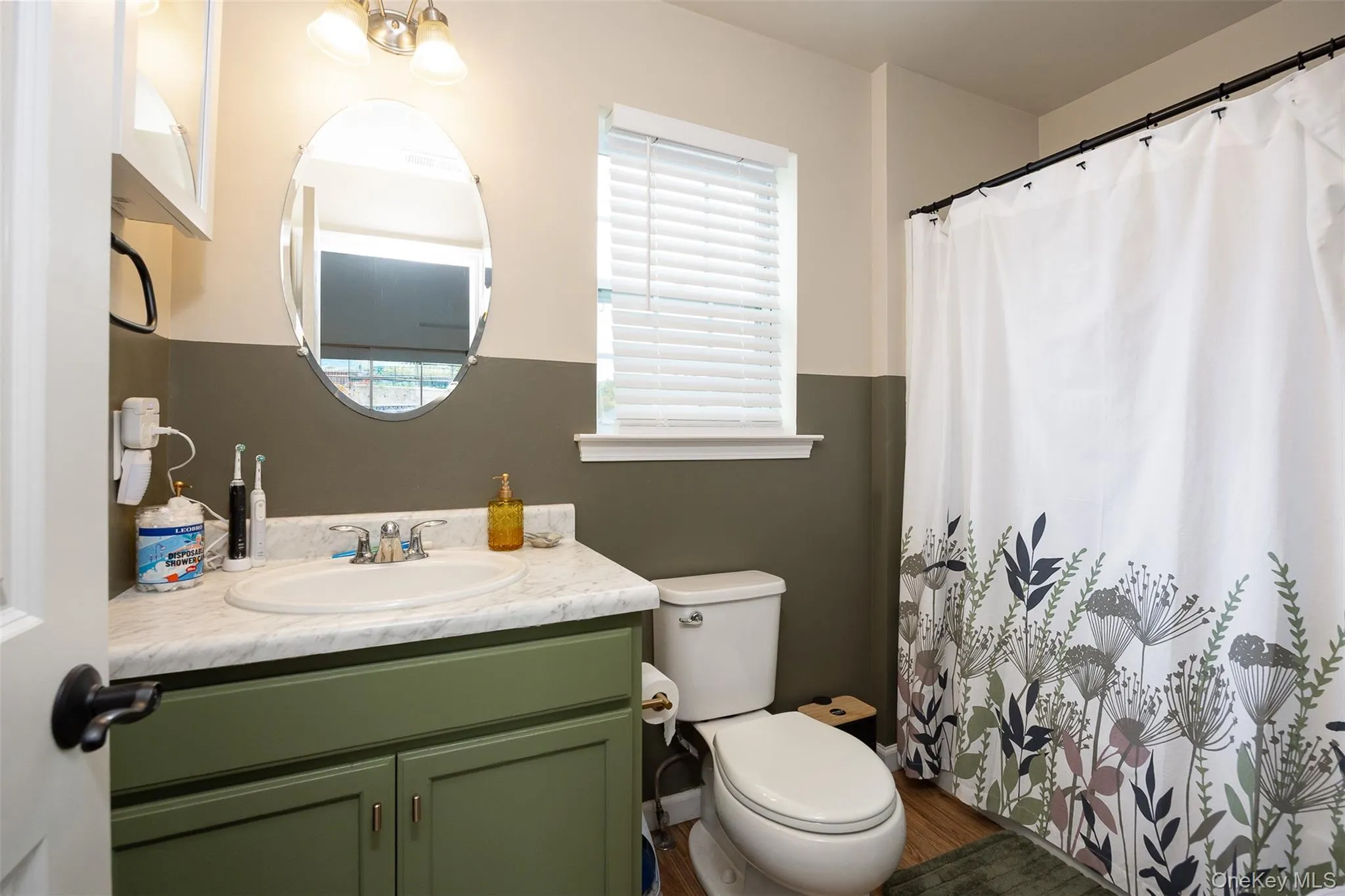 Bathroom featuring a single vanity with an integrated sink, a built-in toilet, and wood-finish flooring Bathroom featuring a single vanity with an integrated sink, a built-in toilet, and wood-finish flooring