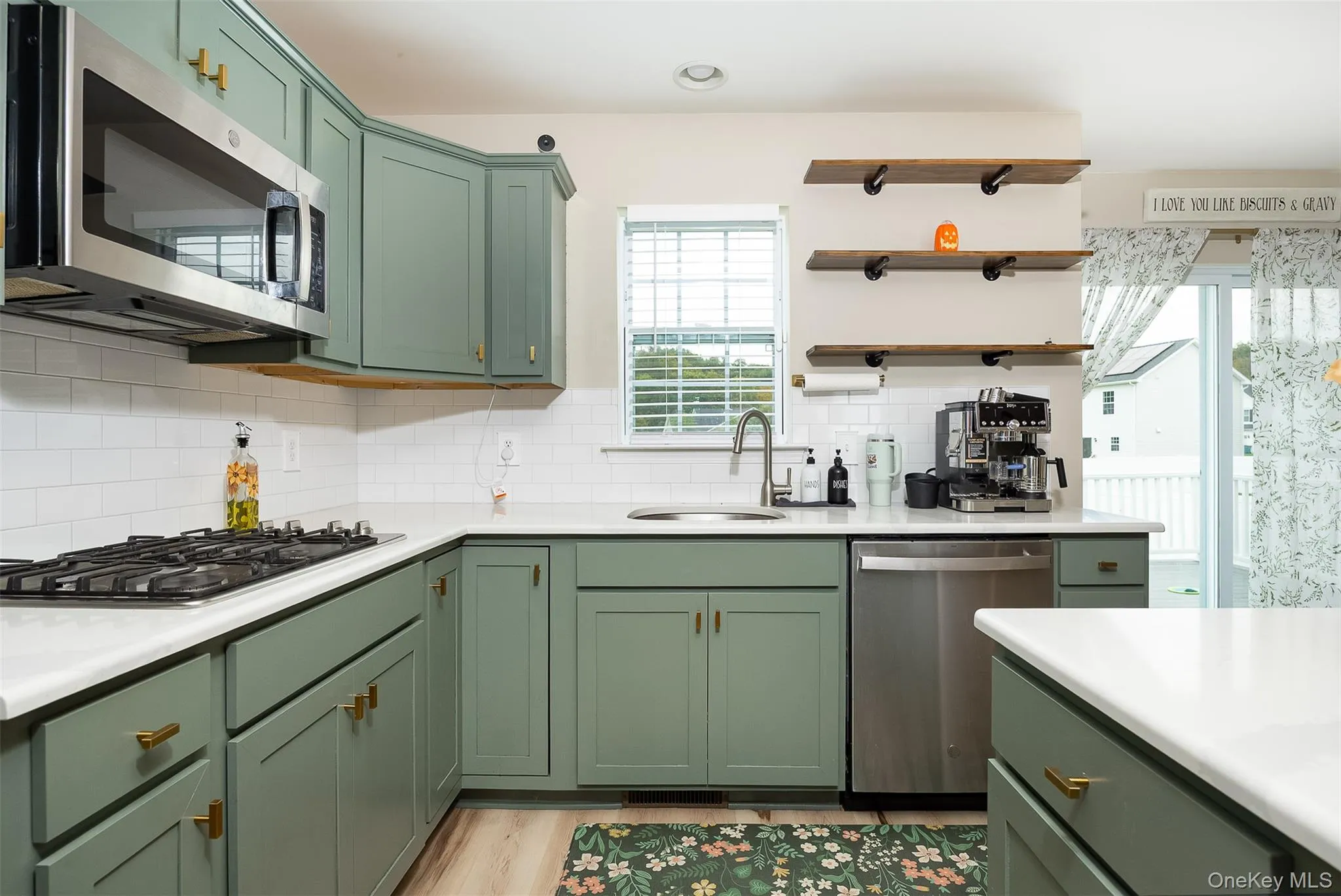 Green shaker-style cabinetry with gold-tone hardware, white countertops, stainless steel appliances, and subway tile backsplash Green shaker-style cabinetry with gold-tone hardware, white countertops, stainless steel appliances, and subway tile backsplash