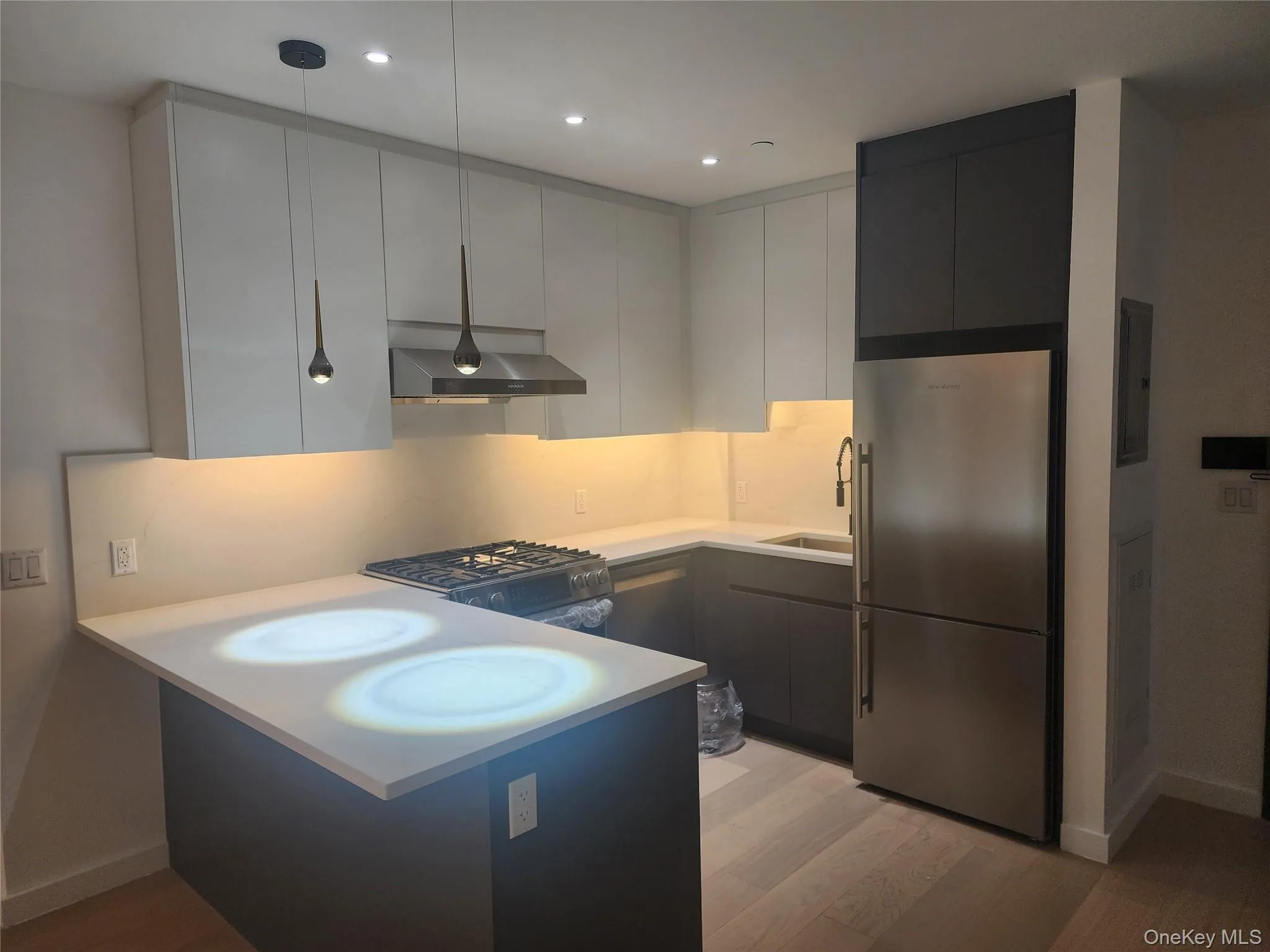 Modern kitchen featuring stainless steel appliances, flat-panel cabinetry, light-toned countertops, a gas range, and wood-finish flooring Modern kitchen featuring stainless steel appliances, flat-panel cabinetry, light-toned countertops, a gas range, and wood-finish flooring