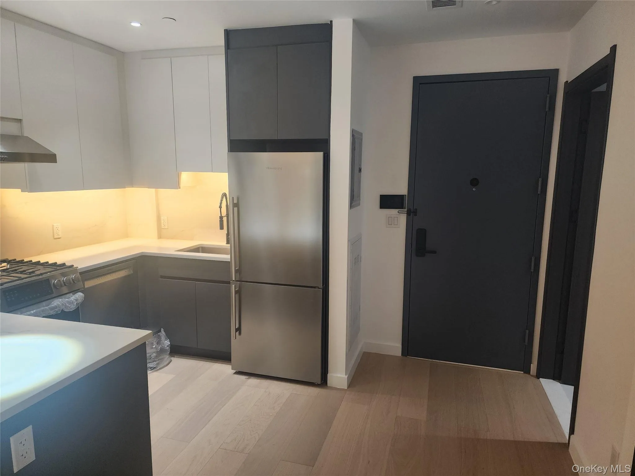 Modern kitchen with integrated stainless steel appliances, light wood-finish flooring, white and gray cabinetry, and under-cabinet lighting Modern kitchen with integrated stainless steel appliances, light wood-finish flooring, white and gray cabinetry, and under-cabinet lighting