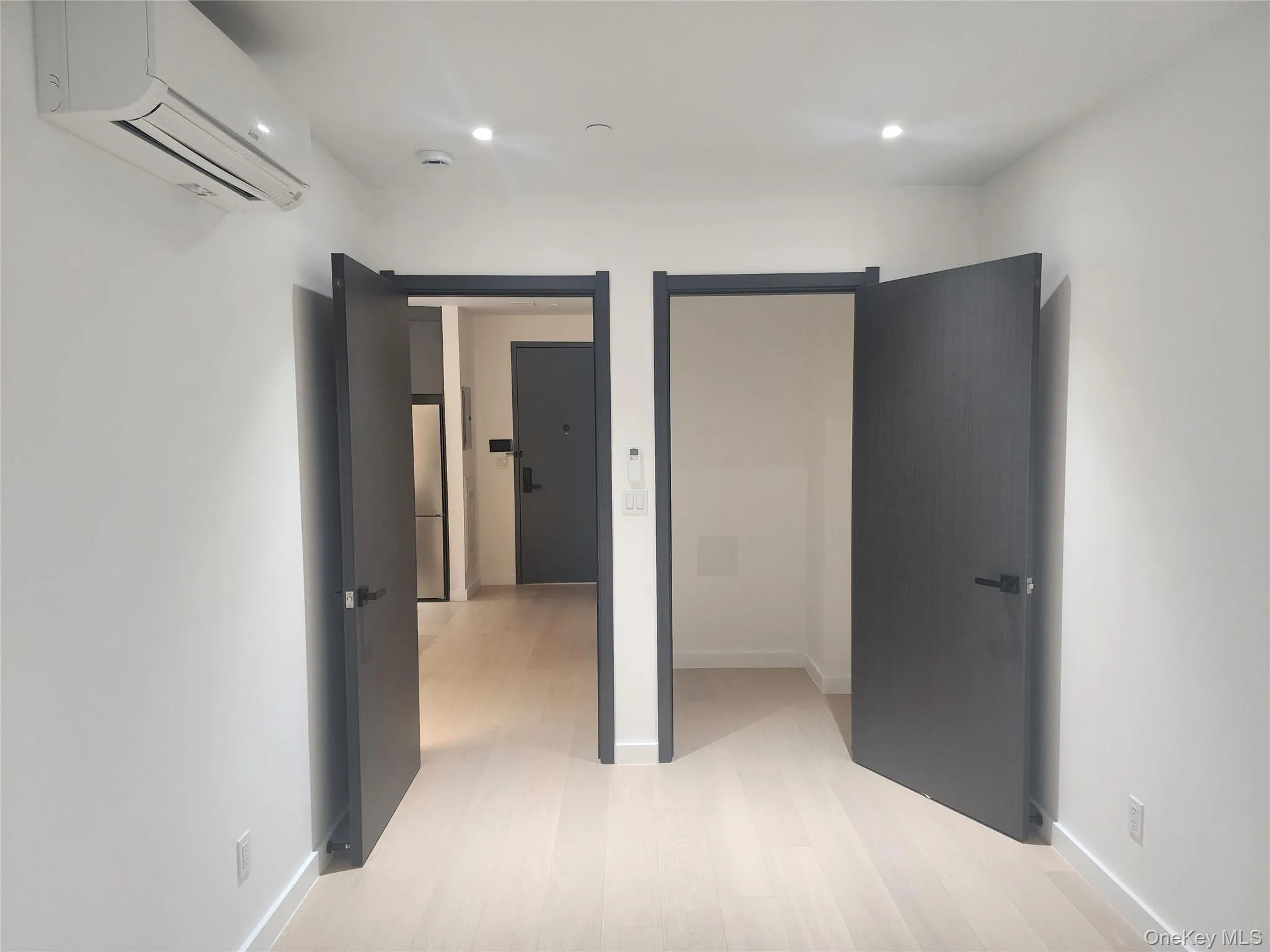 Light wood-finish flooring, recessed lighting, and wall-mounted air conditioning unit Light wood-finish flooring, recessed lighting, and wall-mounted air conditioning unit