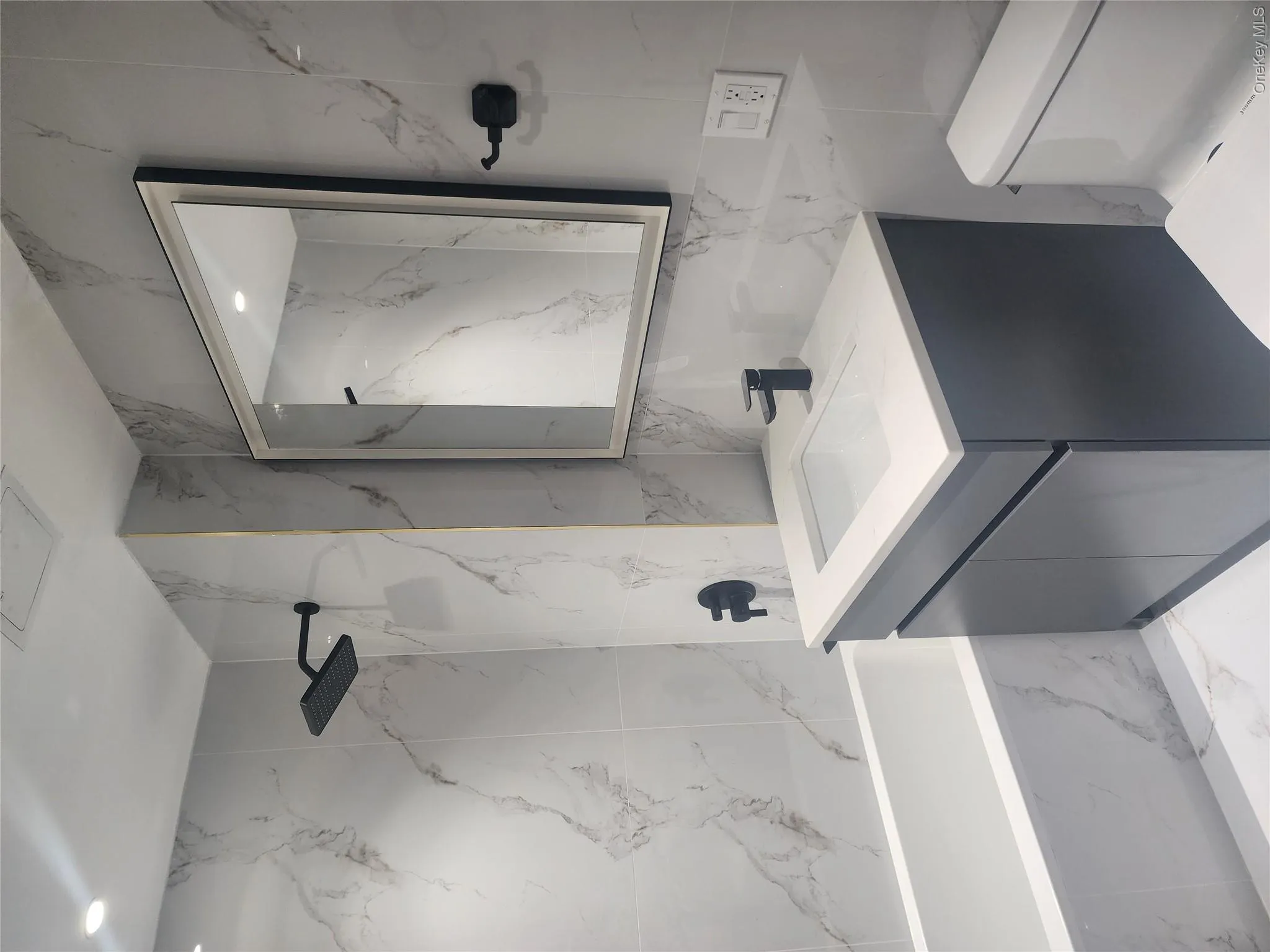 White-tiled bathroom with a built-in tub, matte black shower fixtures, a gray vanity with an integrated sink, and a framed mirror White-tiled bathroom with a built-in tub, matte black shower fixtures, a gray vanity with an integrated sink, and a framed mirror