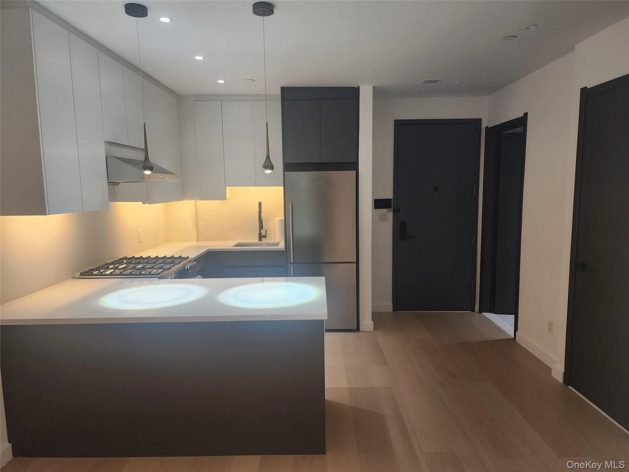 Modern kitchen featuring light wood-finish flooring, two-tone cabinetry, stainless steel appliances, and sleek pendant lighting Modern kitchen featuring light wood-finish flooring, two-tone cabinetry, stainless steel appliances, and sleek pendant lighting