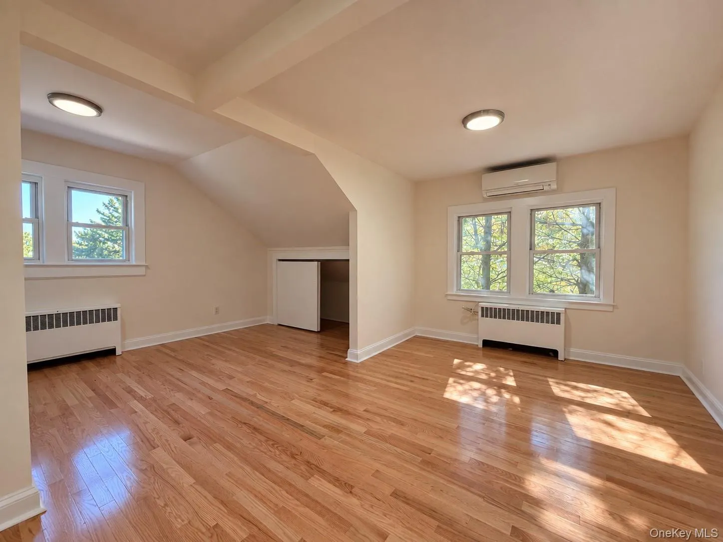 Hardwood flooring, multiple windows, built-in air conditioning unit, ceiling-mounted lighting, and a closet with bifold doors Hardwood flooring, multiple windows, built-in air conditioning unit, ceiling-mounted lighting, and a closet with bifold doors