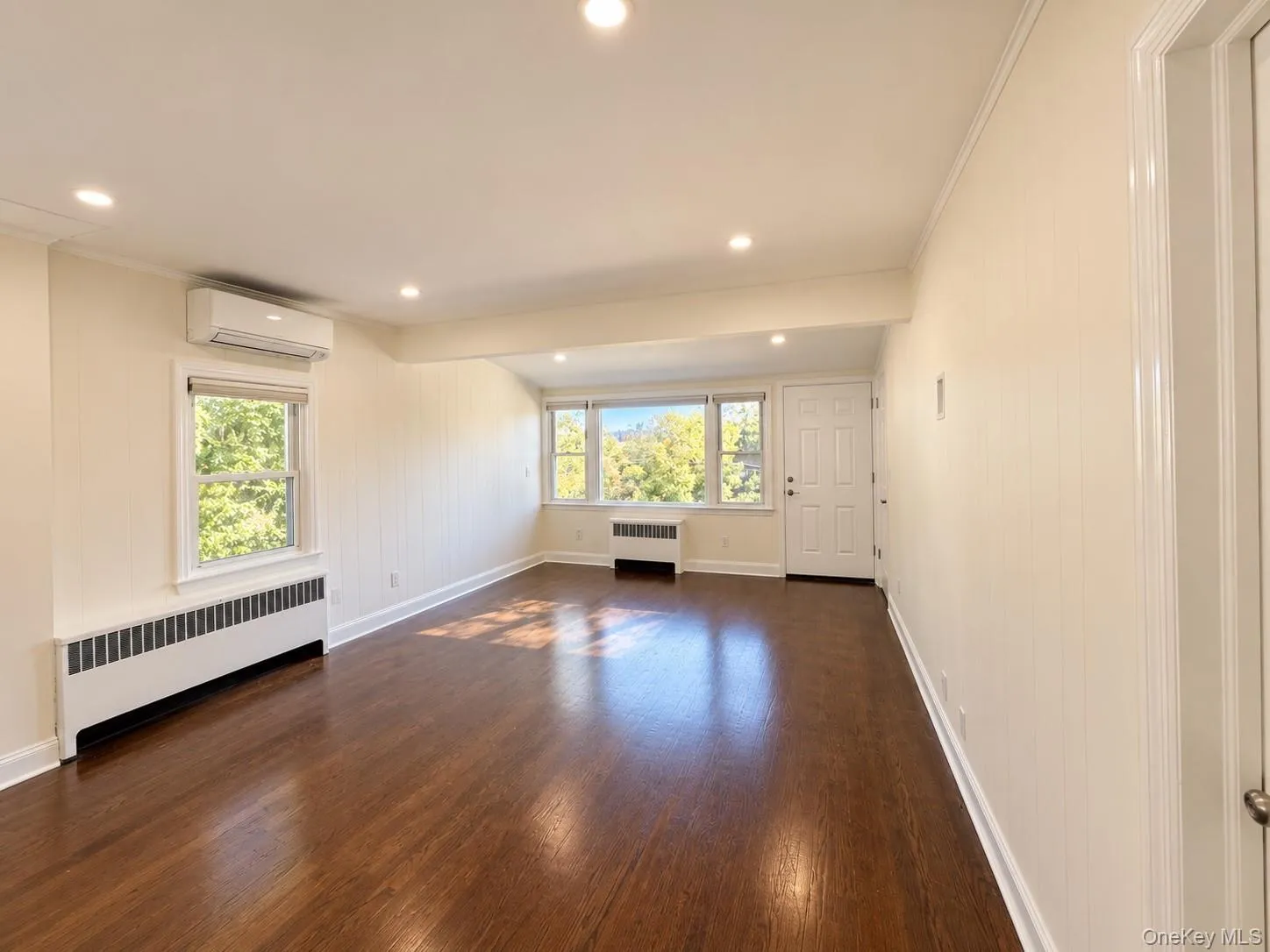 Wood-finish flooring throughout, recessed lighting, white paneled walls, multiple windows, and a split-system air conditioning unit Wood-finish flooring throughout, recessed lighting, white paneled walls, multiple windows, and a split-system air conditioning unit